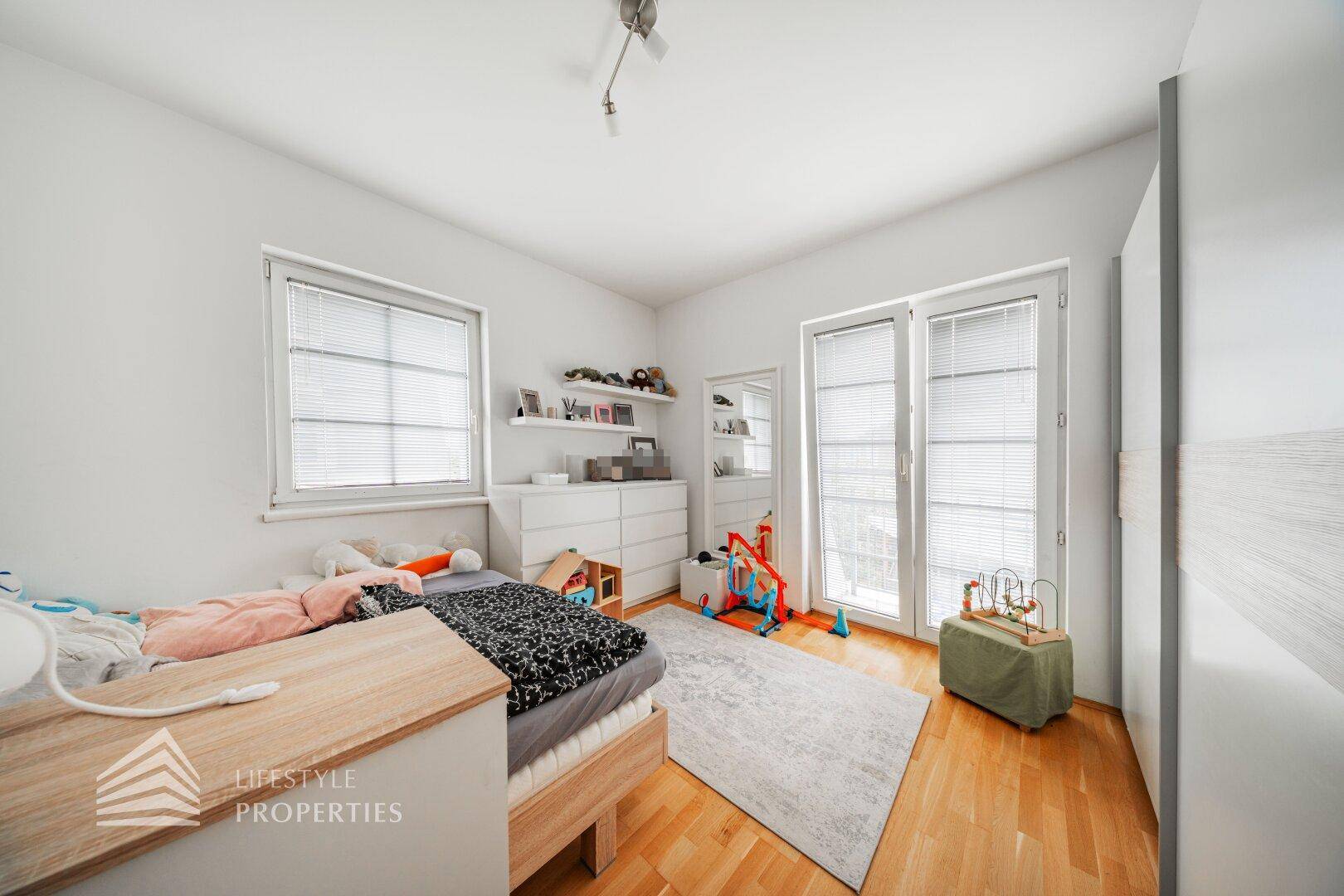 Kinderzimmer mit Parkettboden, Fenster und Zugang zu einem französischen Balkon.
