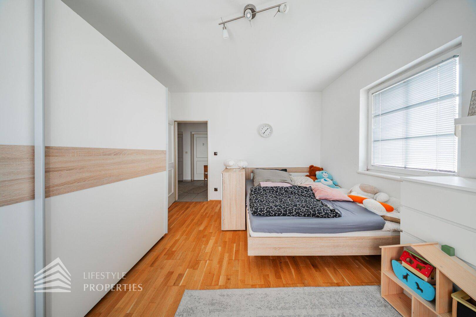 Schlafzimmer mit Parkettboden, großem Kleiderschrank und Fenster für natürliches Licht.