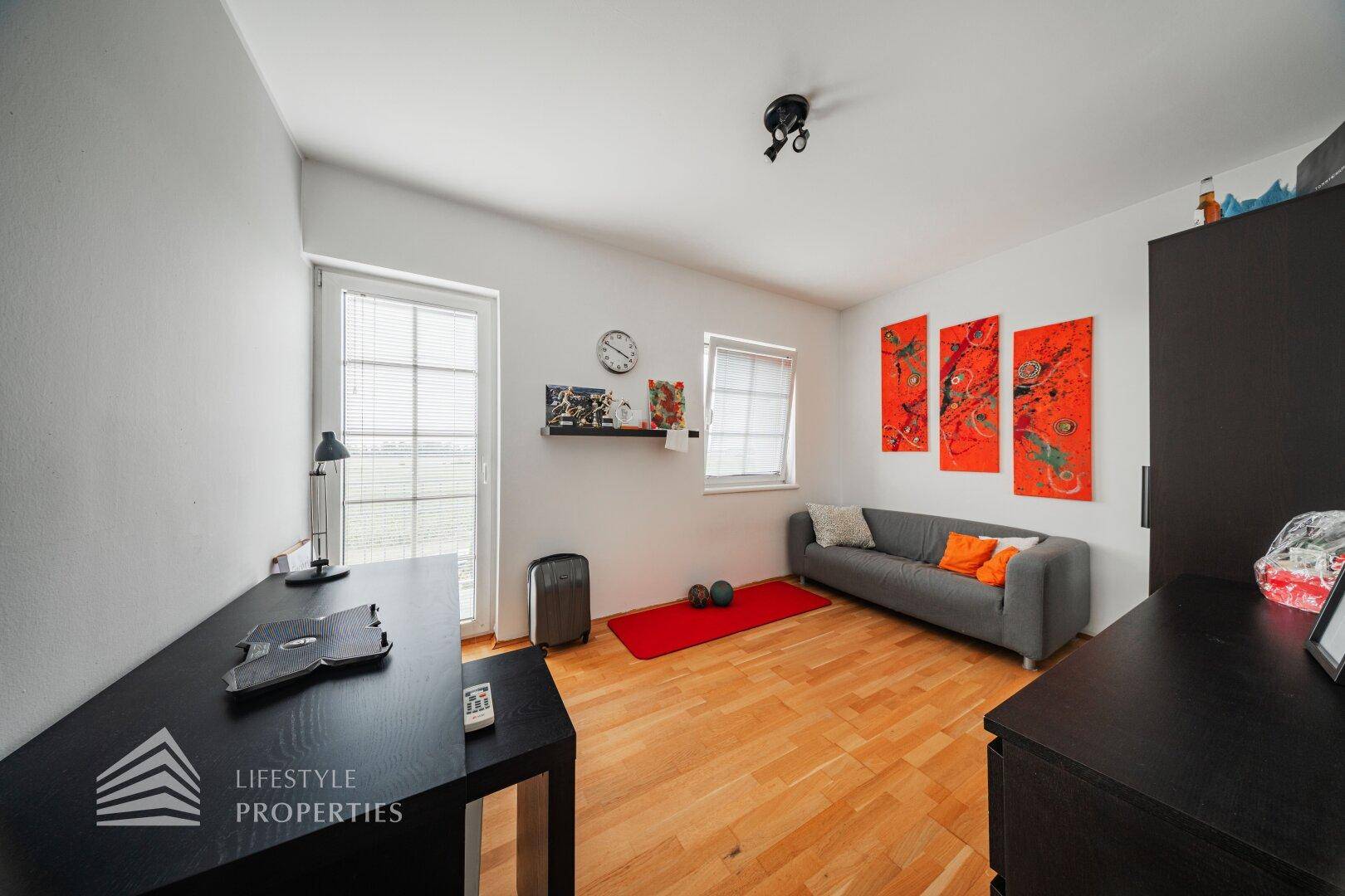 Helles Zimmer mit Parkettboden, Schreibtisch und Zugang zu einem französischen Balkon.