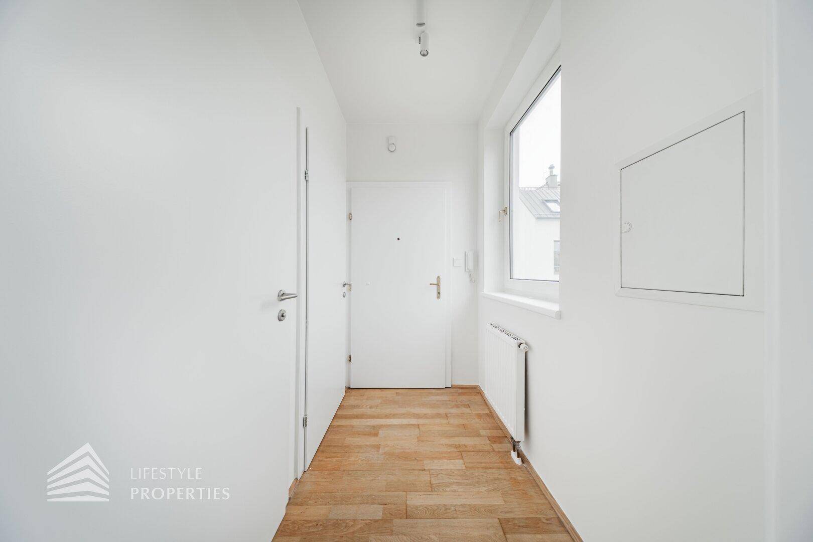Heller Flur mit Holzboden und Fenster, führt zum Eingangsbereich der Wohnung.