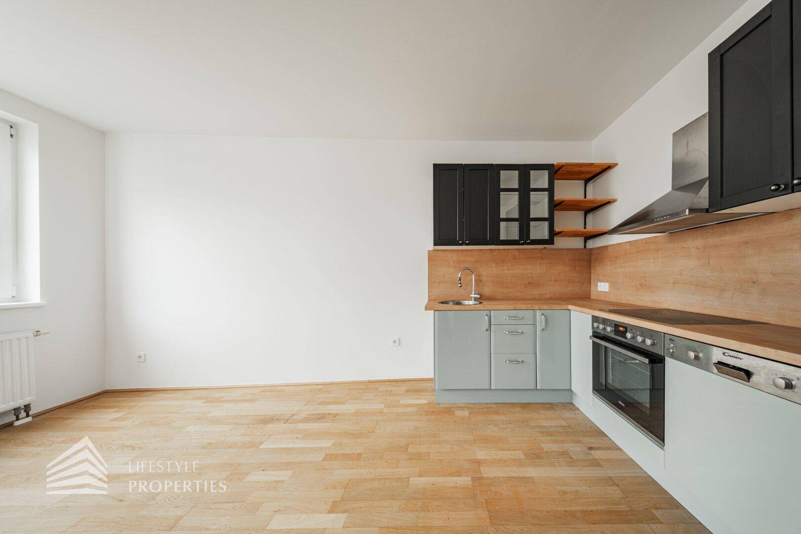 Helle Küche mit Holz-Arbeitsplatte und modernen Geräten, integriert in einen offenen Wohnraum.