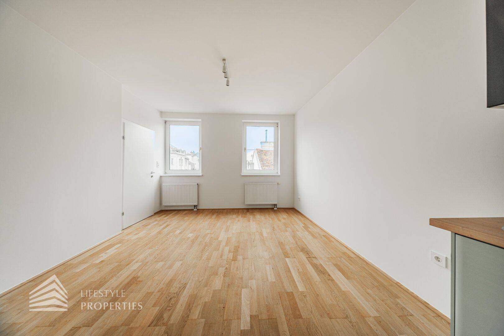 Geräumiger, heller Wohnbereich mit Holzboden und zwei Fenstern, ideal für individuelle Einrichtung.