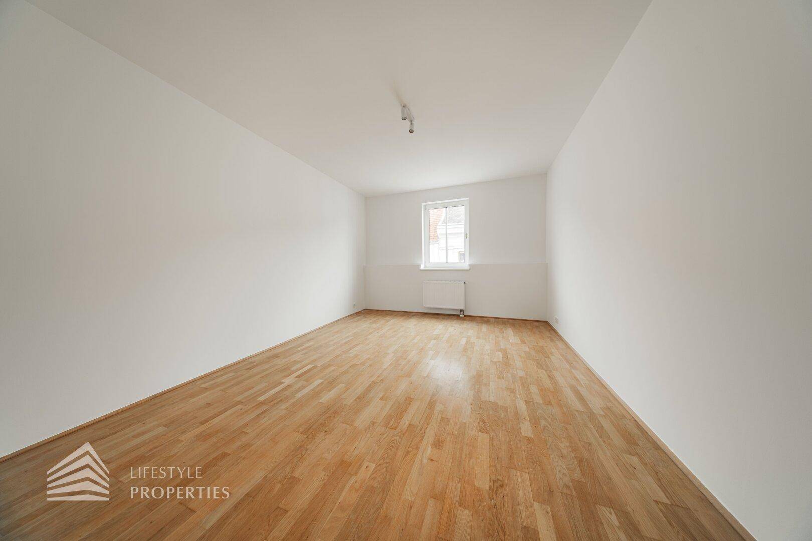 Leerer Raum mit Holzboden und einem Fenster, bietet viel Potenzial für Schlaf- oder Wohnzimmer.