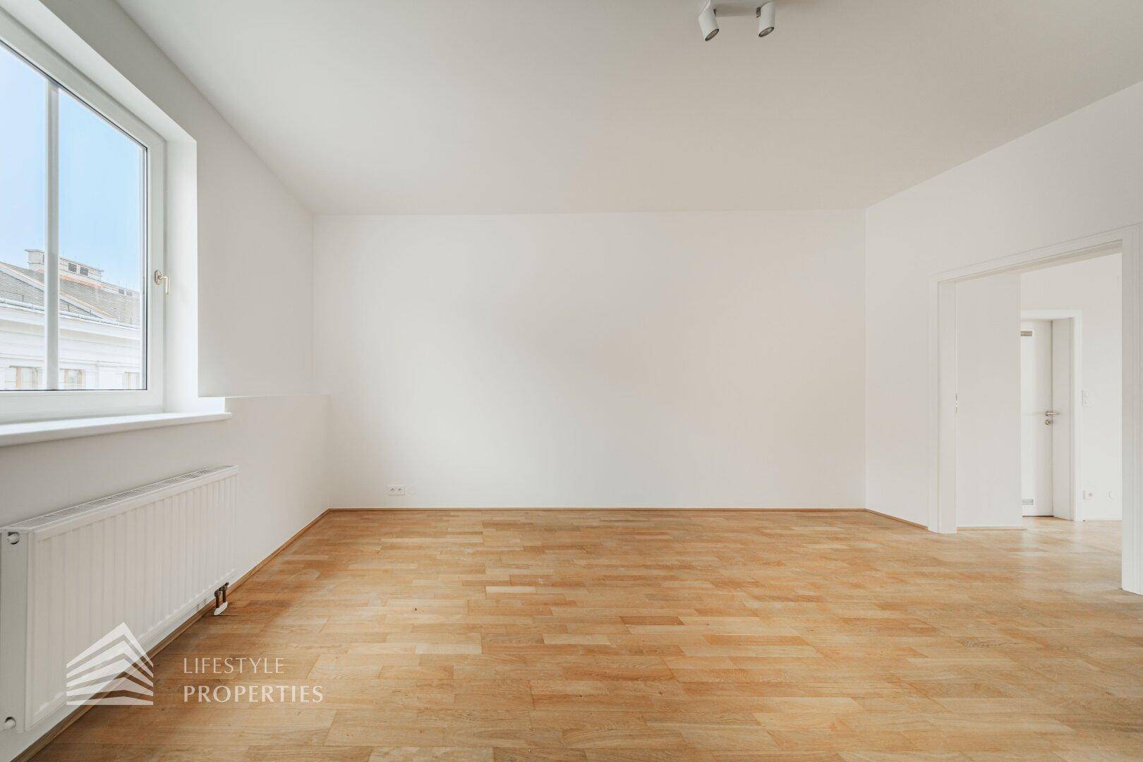 Heller Wohnraum mit Holzboden und großem Fenster, bietet viel Tageslicht und eine angenehme Atmosphäre.