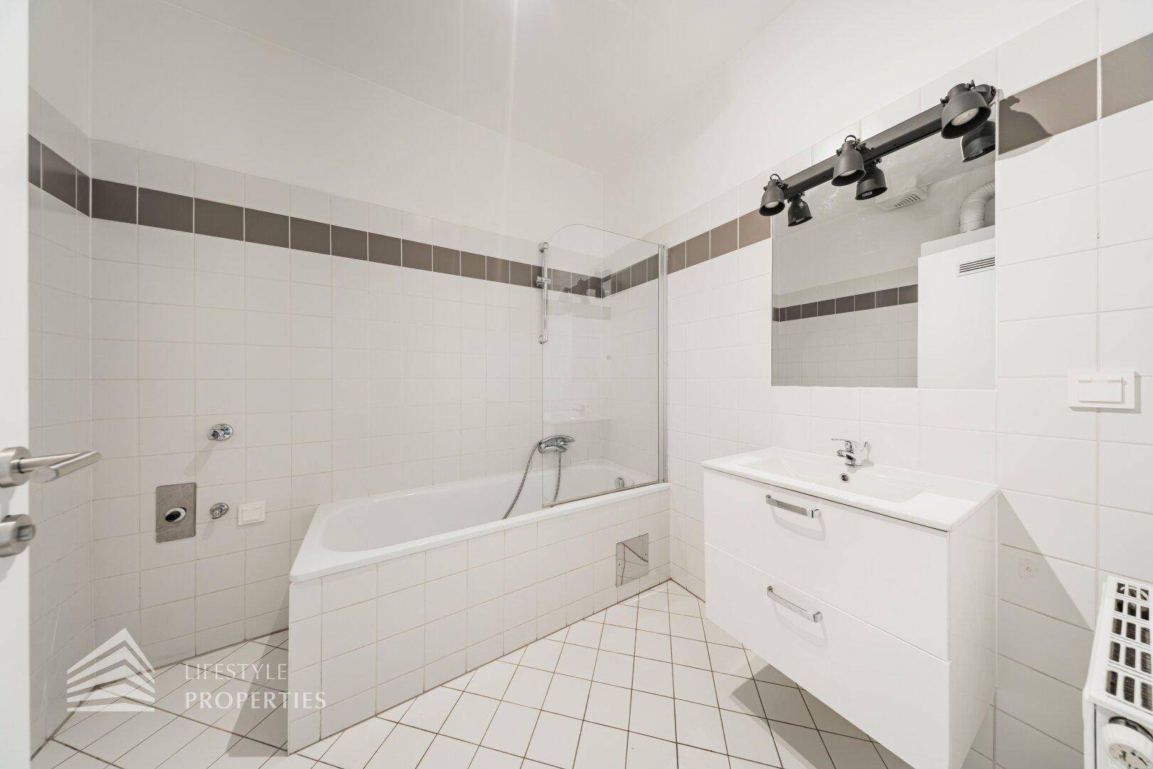Gefliestes Badezimmer mit Badewanne, Duschabtrennung und modernem Waschtisch, in gutem Zustand.