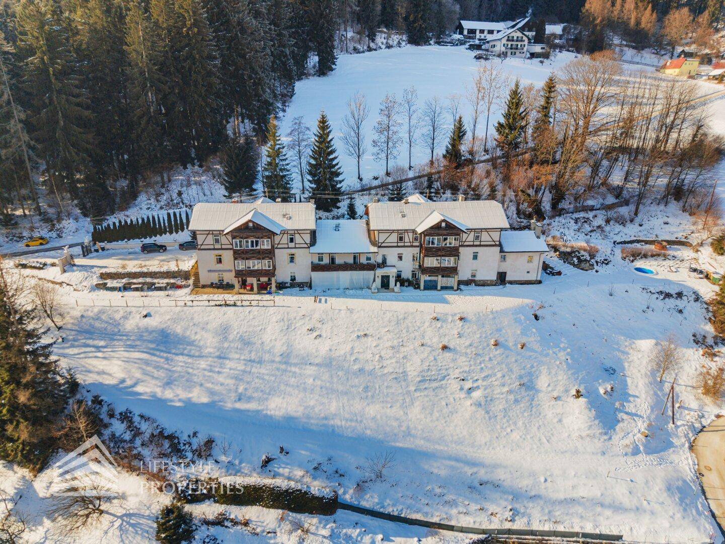 Weitläufige Ansicht des Gebäudes inmitten einer idyllischen, verschneiten Landschaft mit vielen Bäumen.