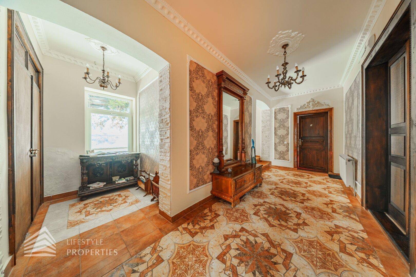 Elegante Eingangshalle mit gemusterten Fliesen, Stuckdecken und traditionellen Holzmöbeln.