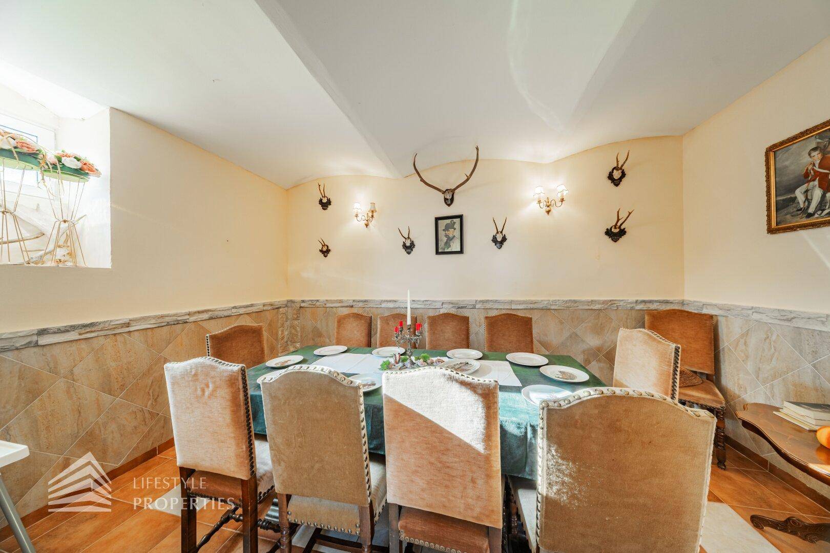 Rustikaler Speisesaal mit großem Esstisch, traditionellen Stühlen und Jagdtrophäen an den Wänden.