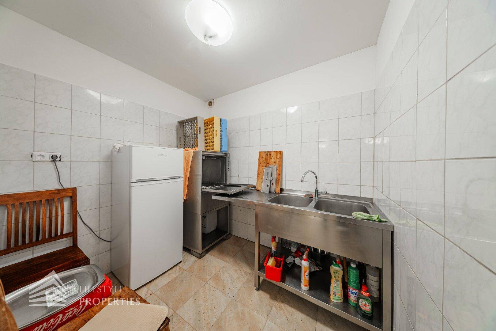 Spülbereich der Großküche mit Doppelwaschbecken aus Edelstahl und einem Kühlschrank.