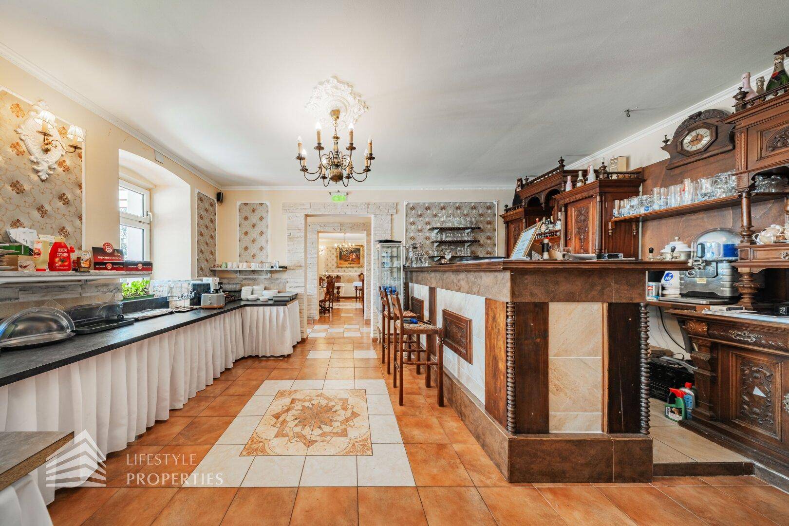 Frühstücksraum mit Buffettheke, traditioneller Bar und Blick in den angrenzenden Speisesaal.