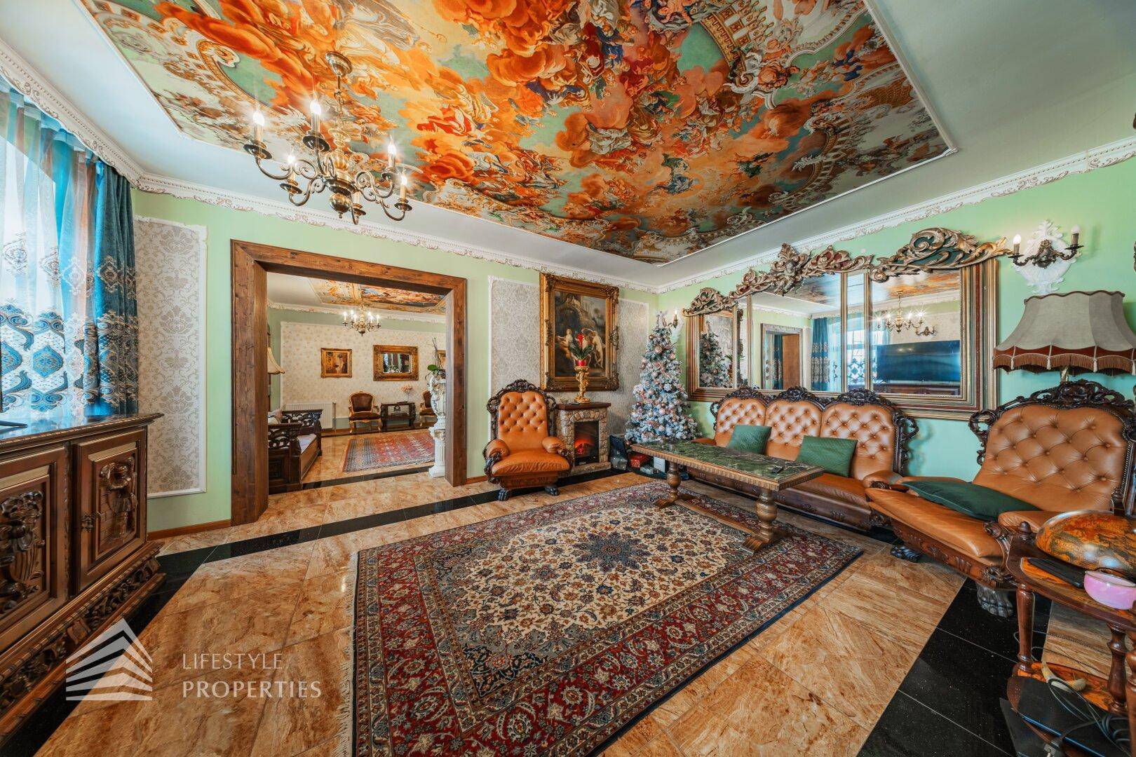 Geräumiger Wohnsalon mit opulenten Möbeln, einem großen Spiegel und dem beeindruckenden Deckengemälde.