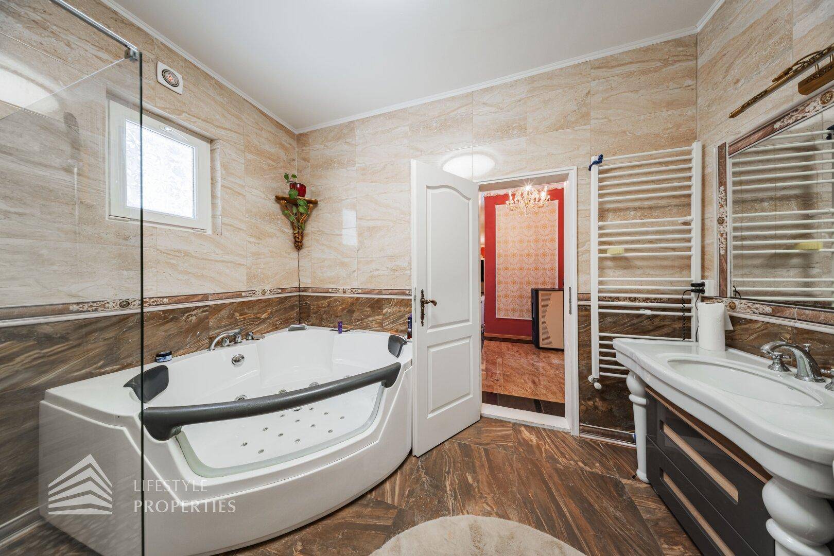 Badezimmer mit Eckbadewanne, Fenster und beheiztem Handtuchhalter, alles in warmen Fliesenfarben.