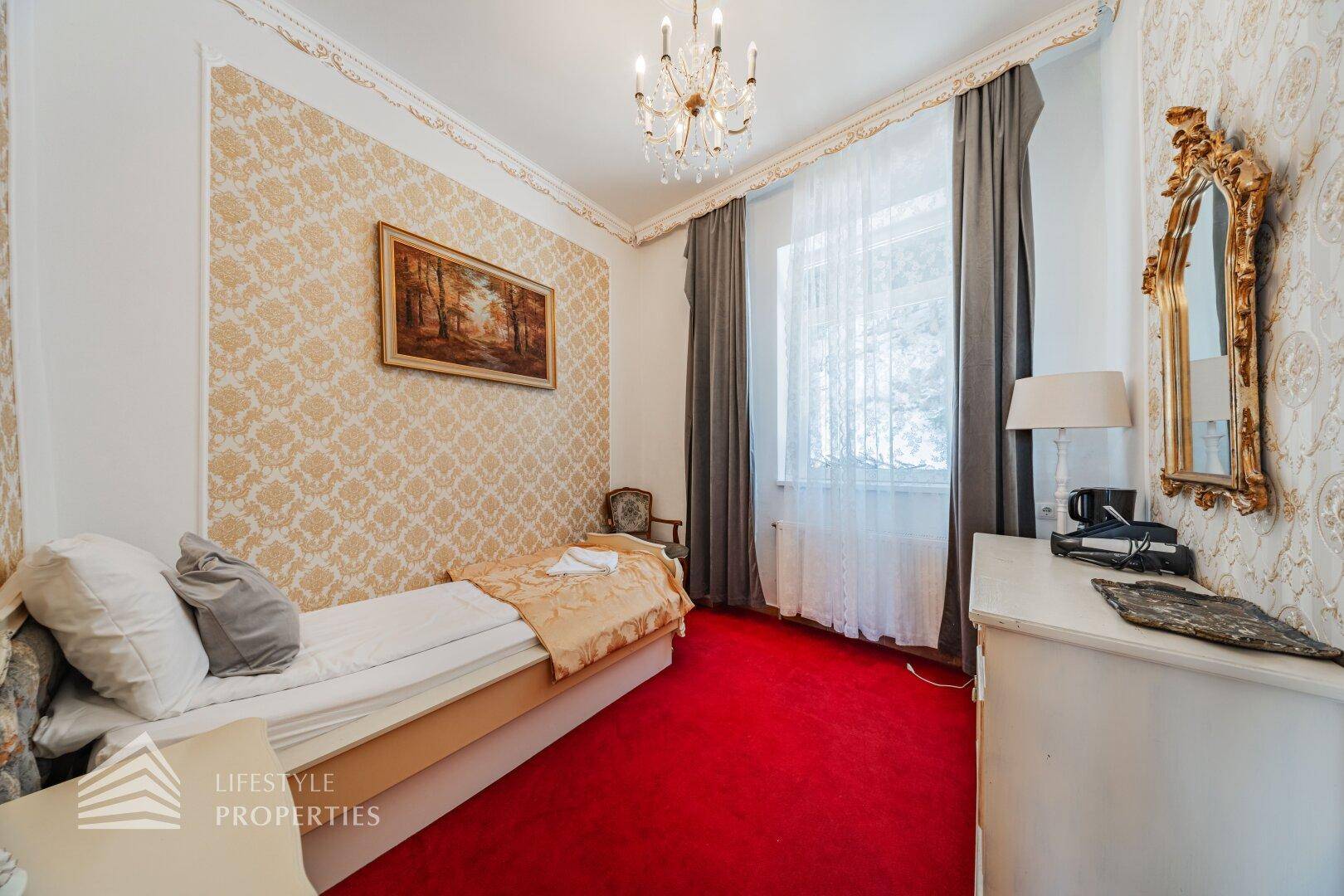 Kleines Schlafzimmer mit Einzelbett, rotem Teppich, gemusterter Tapete und einem Fenster.