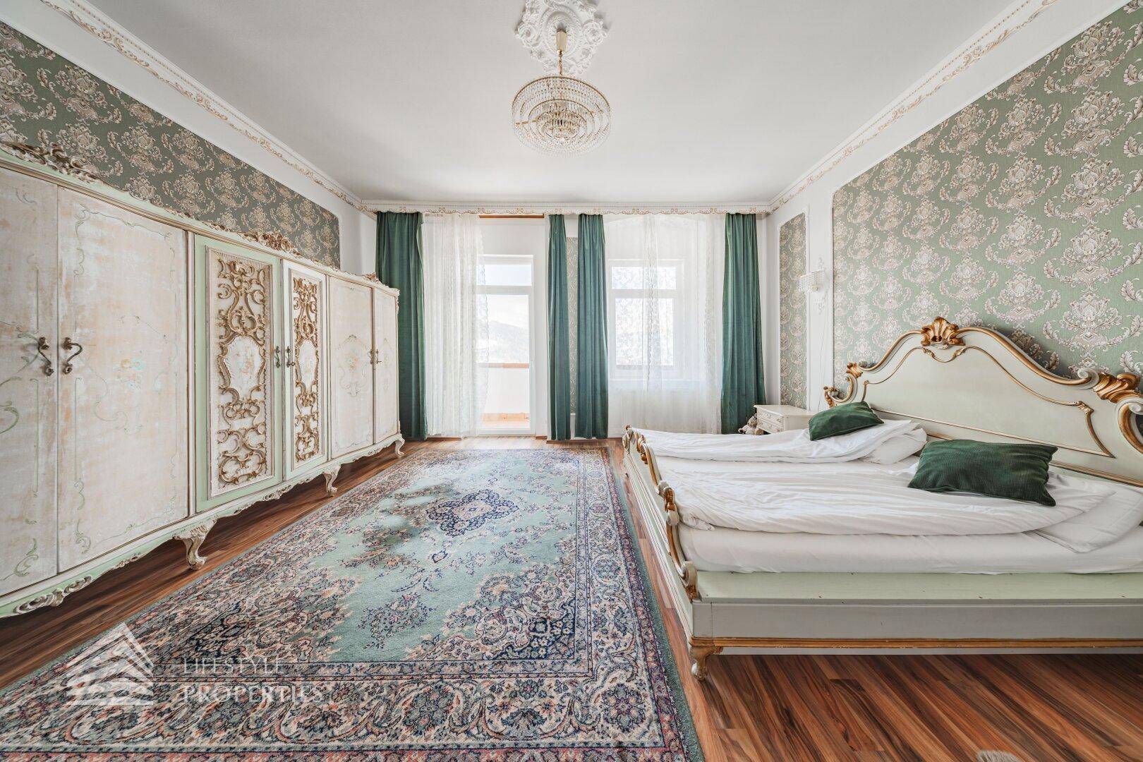 Schlafzimmer mit zwei Einzelbetten, großem verzierten Kleiderschrank und grün gemusterter Tapete.