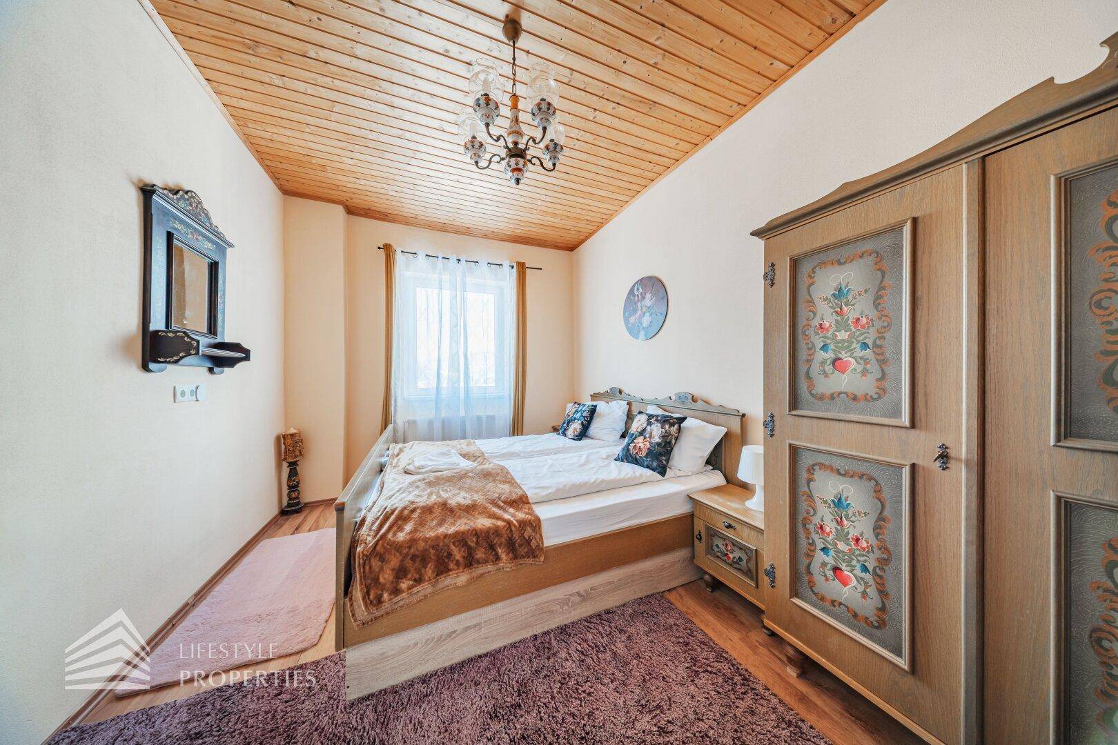 Schlafzimmer mit Doppelbett, bemaltem Kleiderschrank und einer rustikalen Holzdecke.