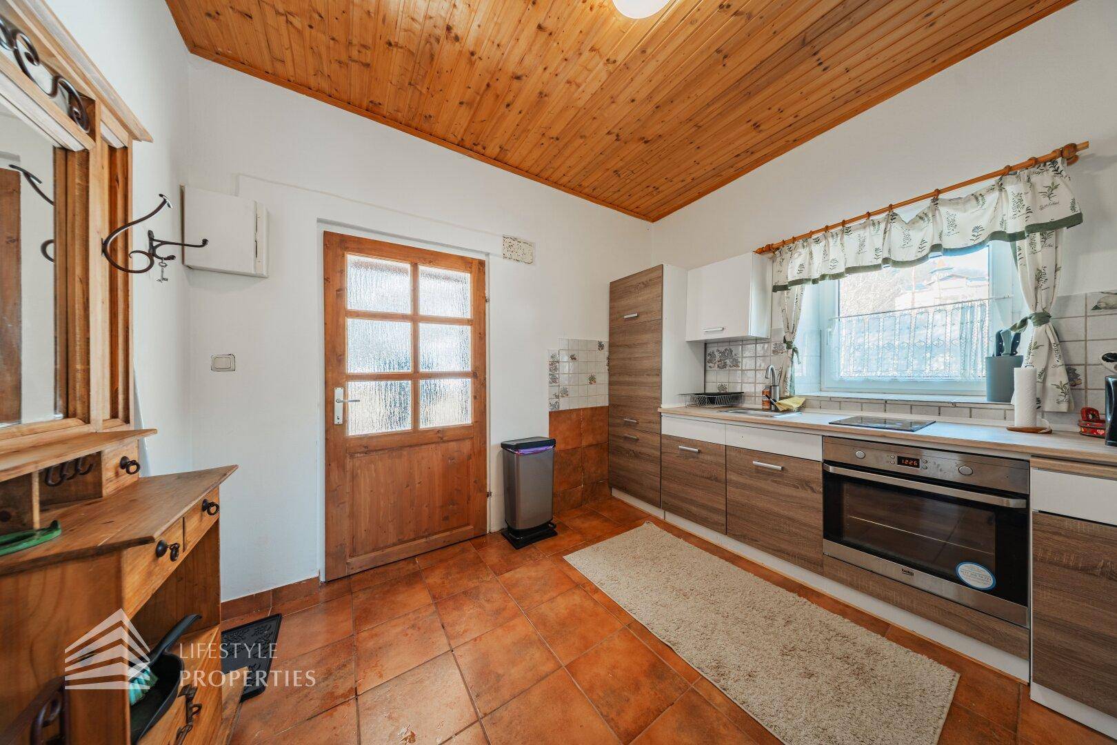 Küche mit Holzschränken, Einbauofen, Spüle und einer rustikalen Holzdecke.
