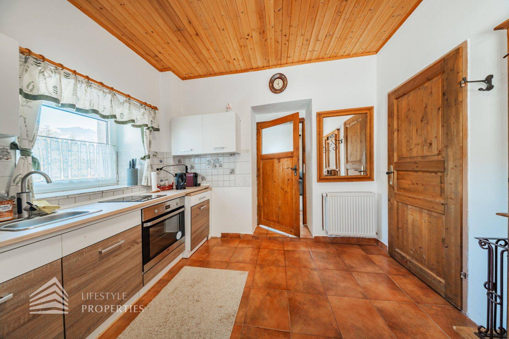 Küche mit Holzschränken, Einbaugeräten und einer traditionellen Holztür.
