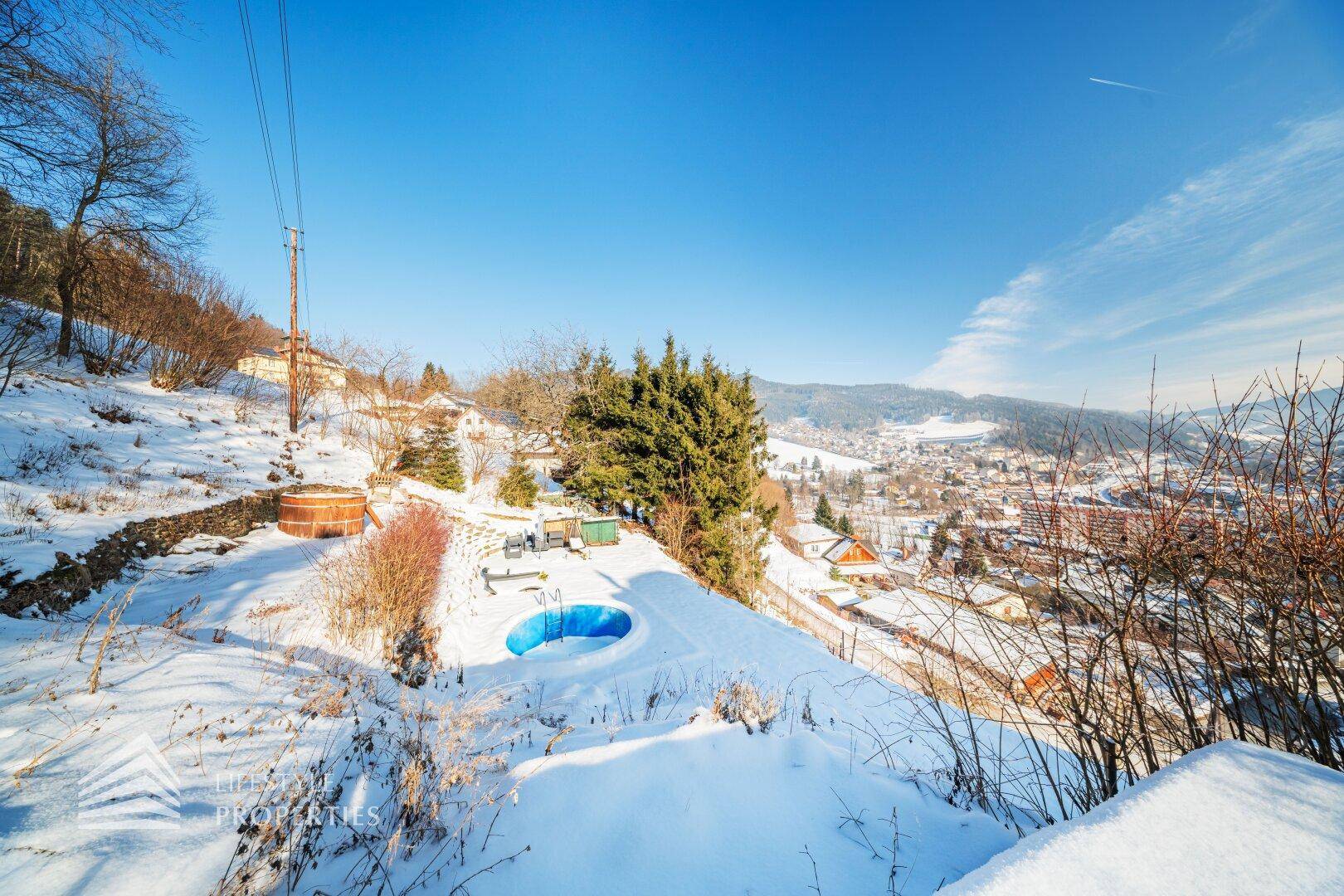 Verschneiter Gartenbereich mit kleinem Pool und Whirlpool, mit Blick auf die Stadt.