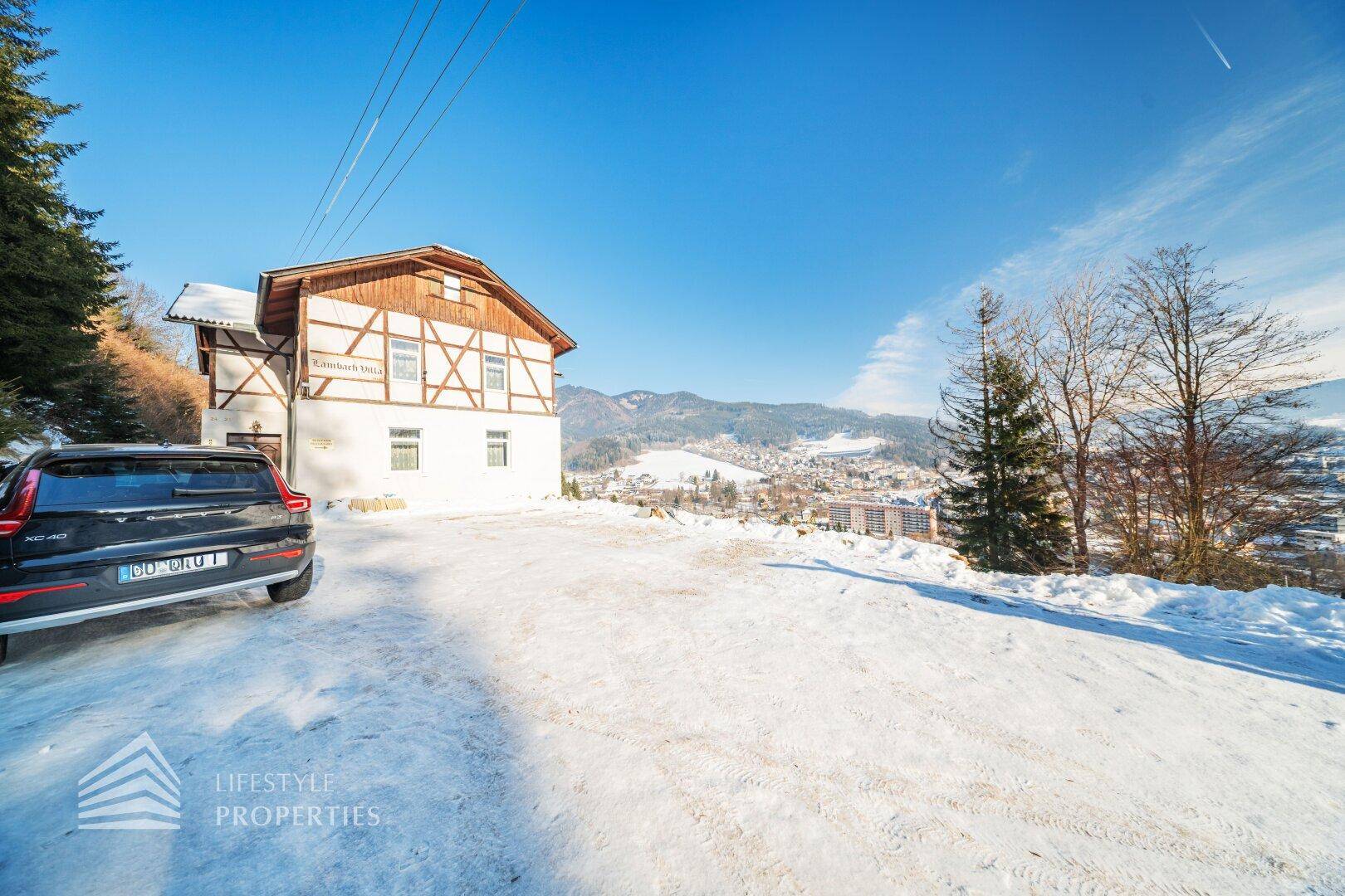 Außenansicht eines traditionellen Gebäudes mit Auto auf verschneitem Parkplatz und Bergblick.