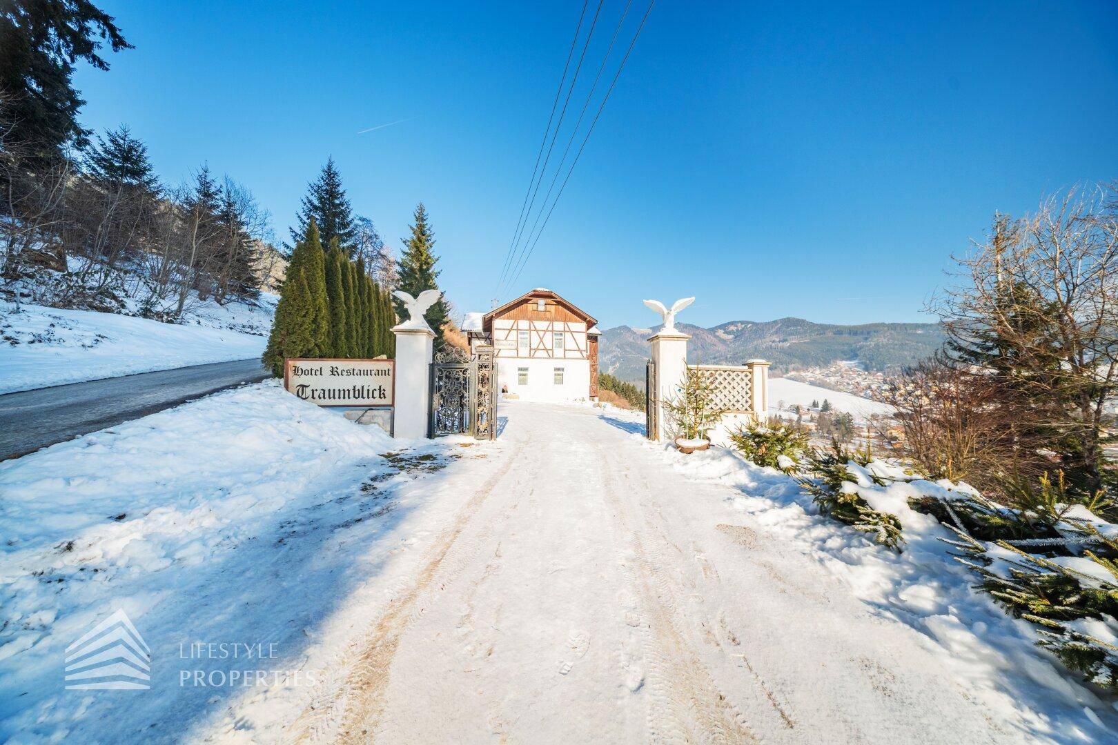 Eingangsbereich eines Hotels mit verschneiter Auffahrt und traditionellem Gebäude im Hintergrund.