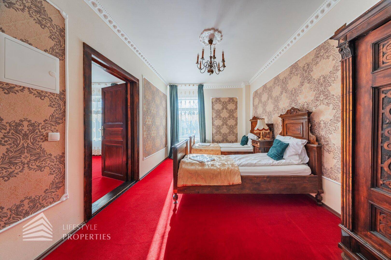 Geräumiges Schlafzimmer mit zwei Einzelbetten, rotem Teppich und gemusterter Tapete im klassischen Stil.