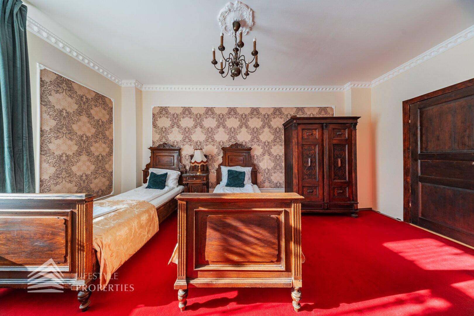 Klassisches Schlafzimmer mit zwei Einzelbetten, großem Holzschrank und rotem Teppichboden.