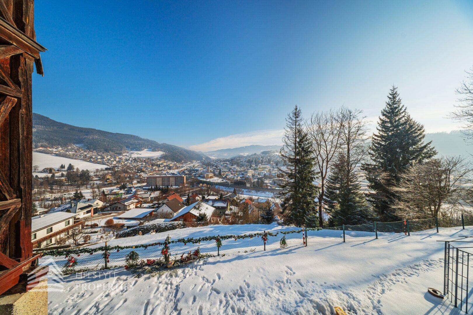 Panoramablick über eine verschneite Landschaft und eine Stadt im Tal unter klarem blauem Himmel.