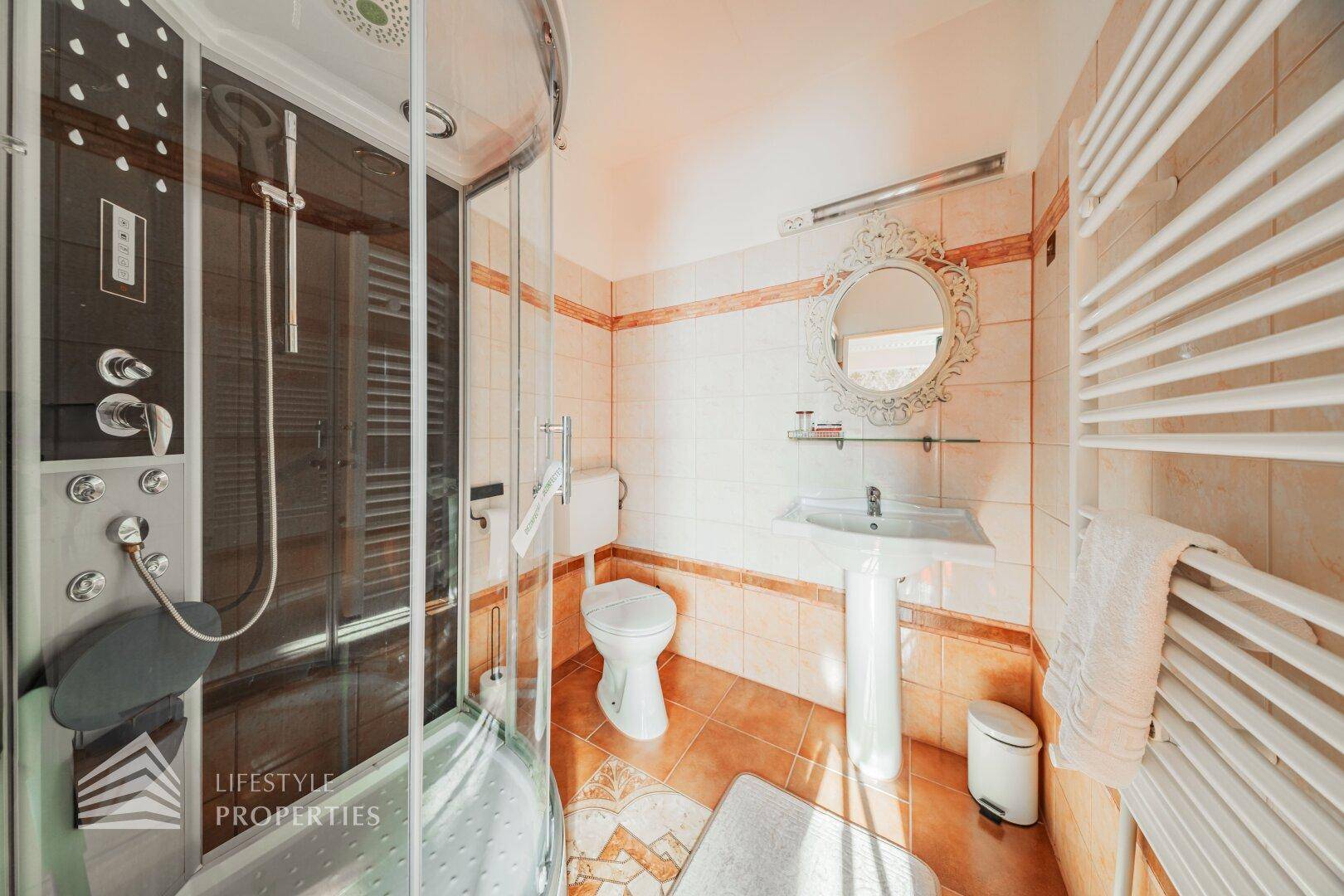 Badezimmer mit moderner Duschkabine, WC und Waschbecken, ausgestattet mit Fliesen in warmen Farbtönen.