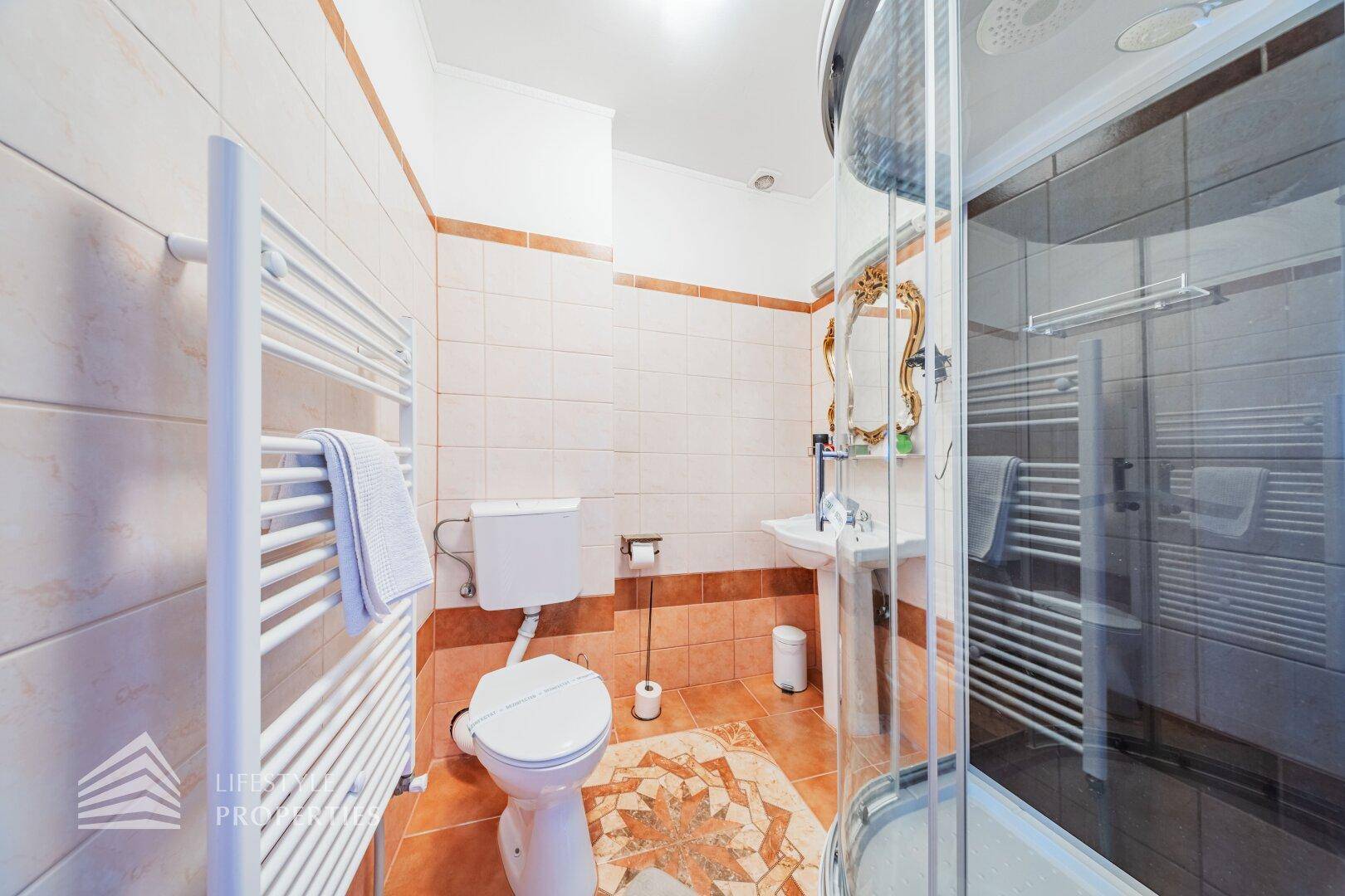 Helles Badezimmer mit WC, Waschbecken und Duschkabine, ergänzt durch einen praktischen Handtuchheizkörper.