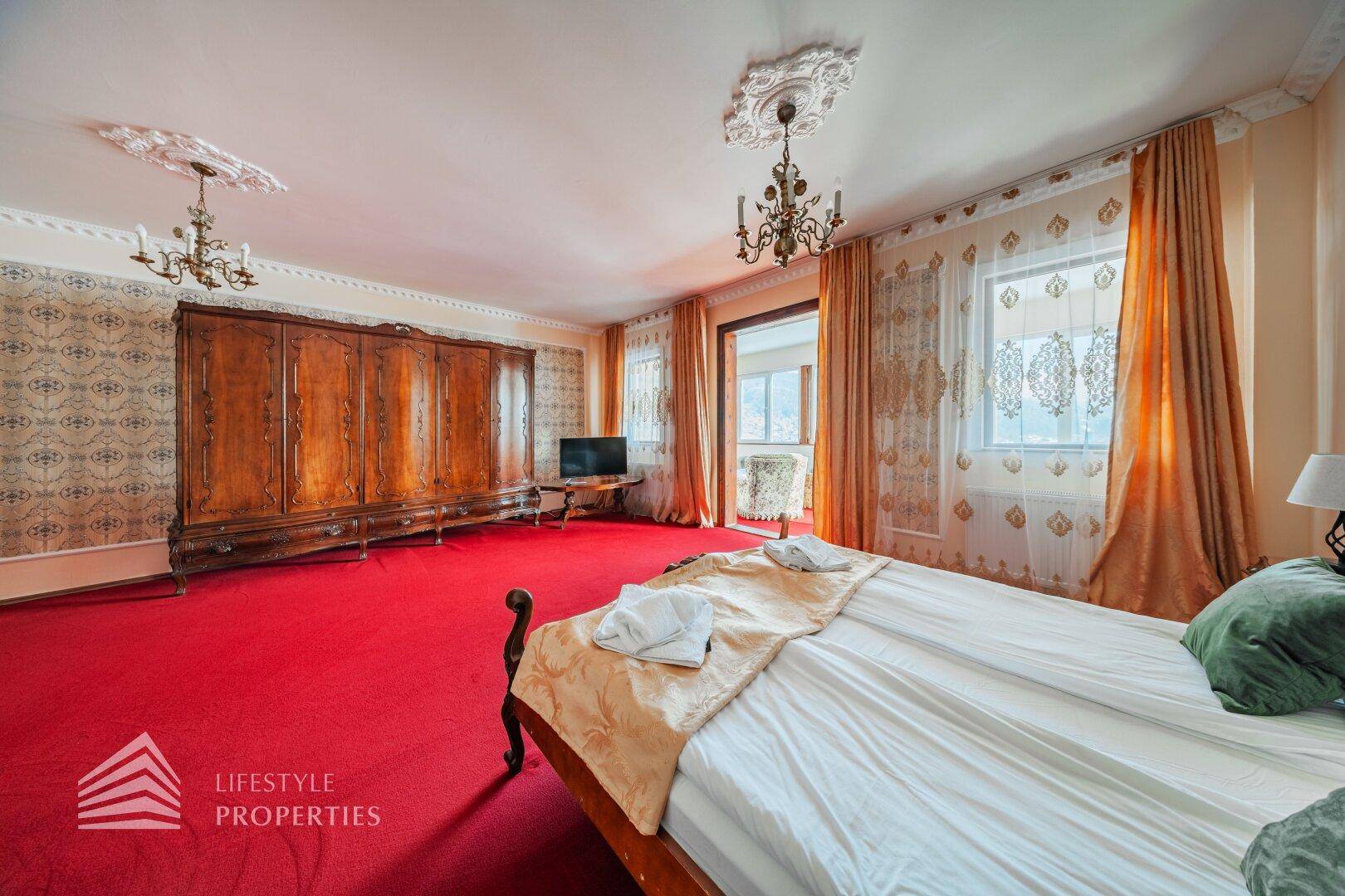 Weitläufiges Schlafzimmer mit rotem Teppich, Doppelbett und Blick auf die verschneite Landschaft durch große Fenster.