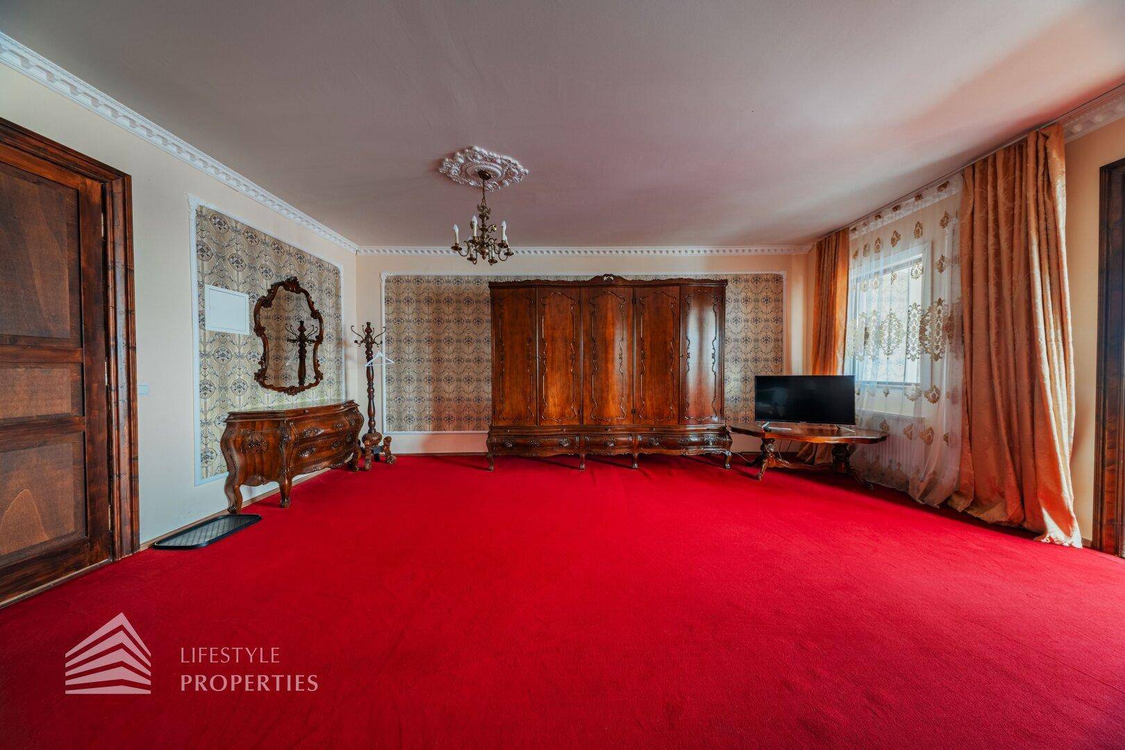 Schlafzimmer mit rotem Teppich, großem Holzschrank und Kommode, klassisch eingerichtet und gut beleuchtet.