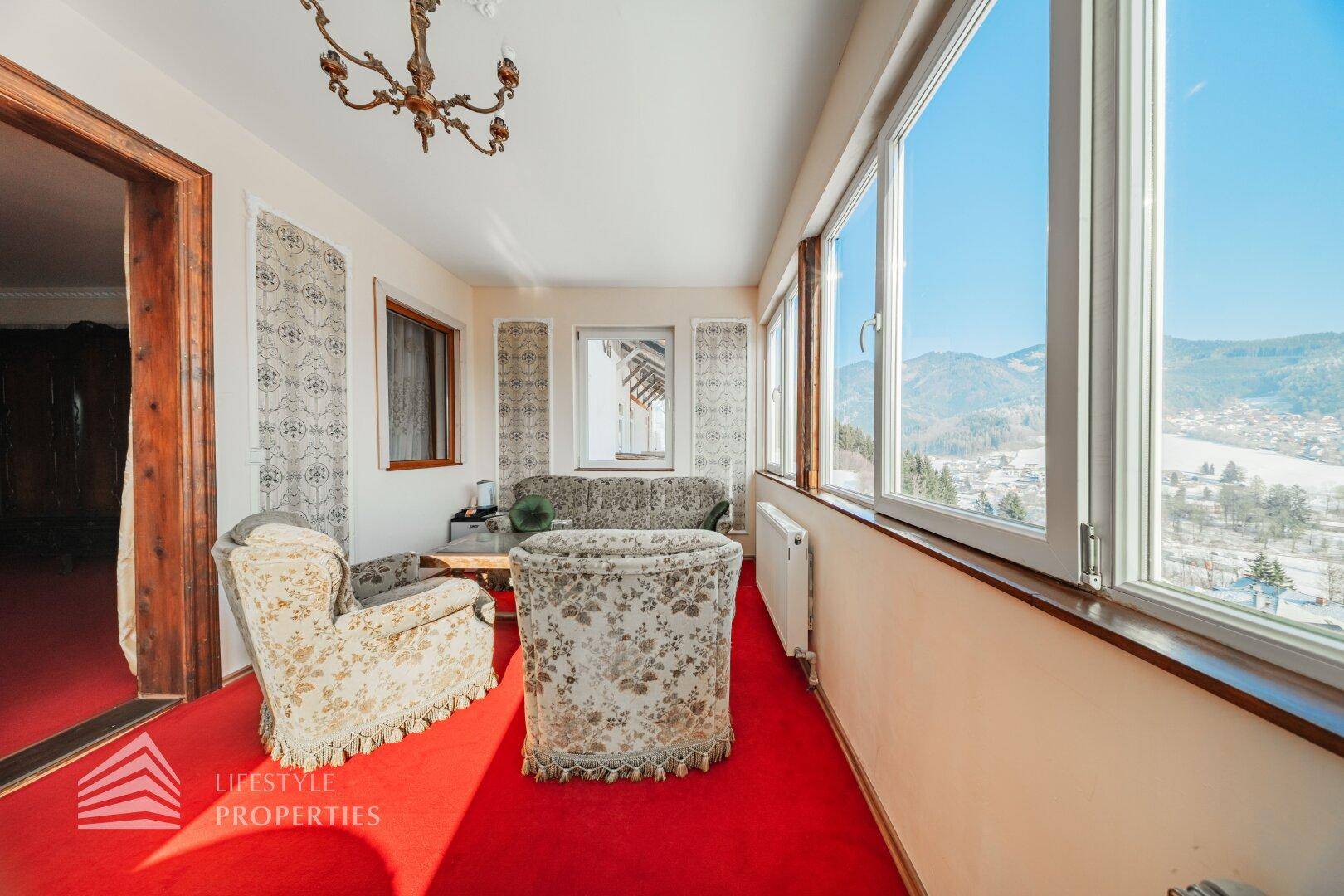 Helles Wohnzimmer mit rotem Teppich und großen Fenstern, die einen weiten Blick auf die Landschaft bieten.