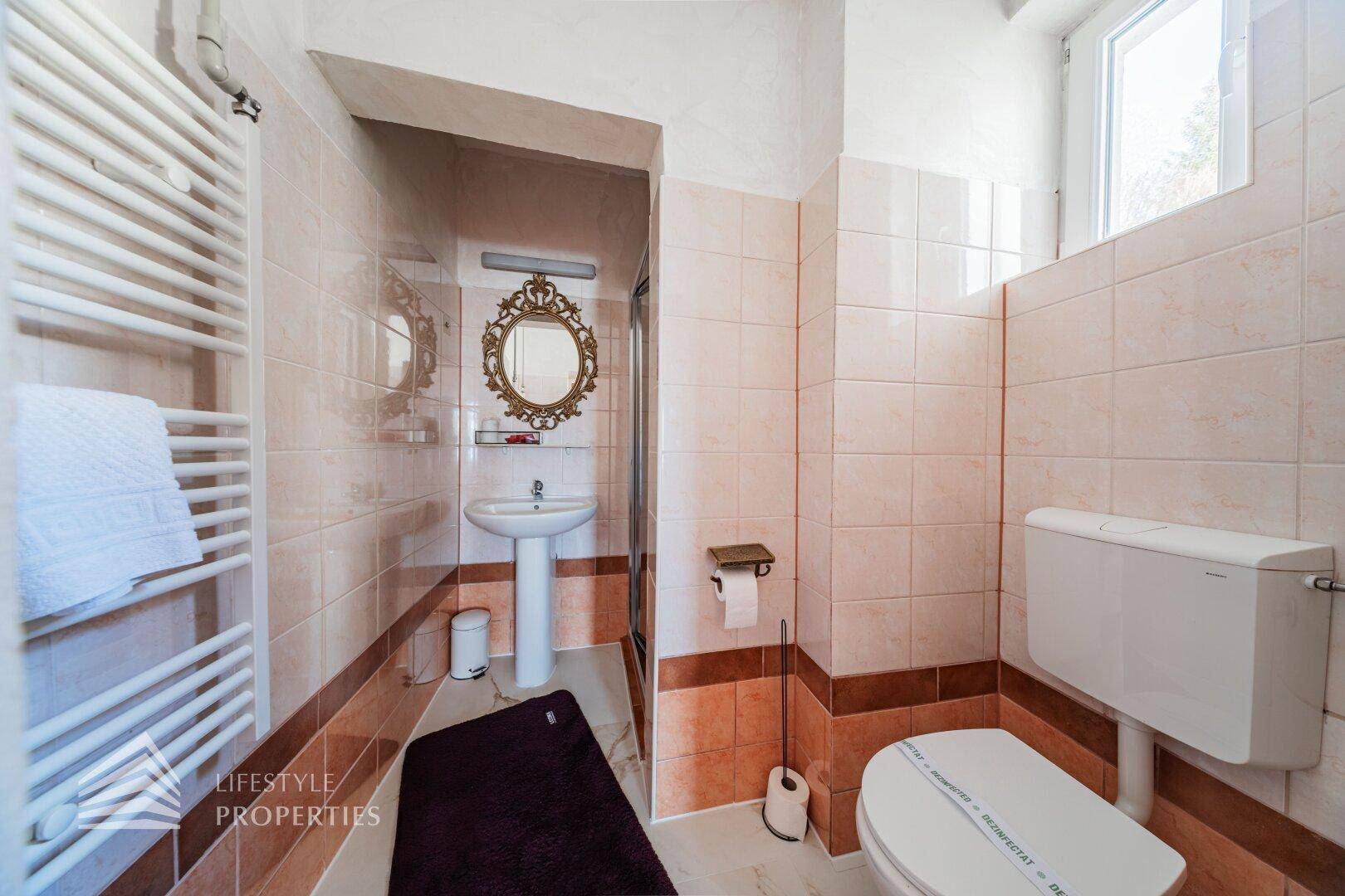 Gefliestes Badezimmer mit WC, Waschbecken und Duschbereich, hell und funktional eingerichtet.