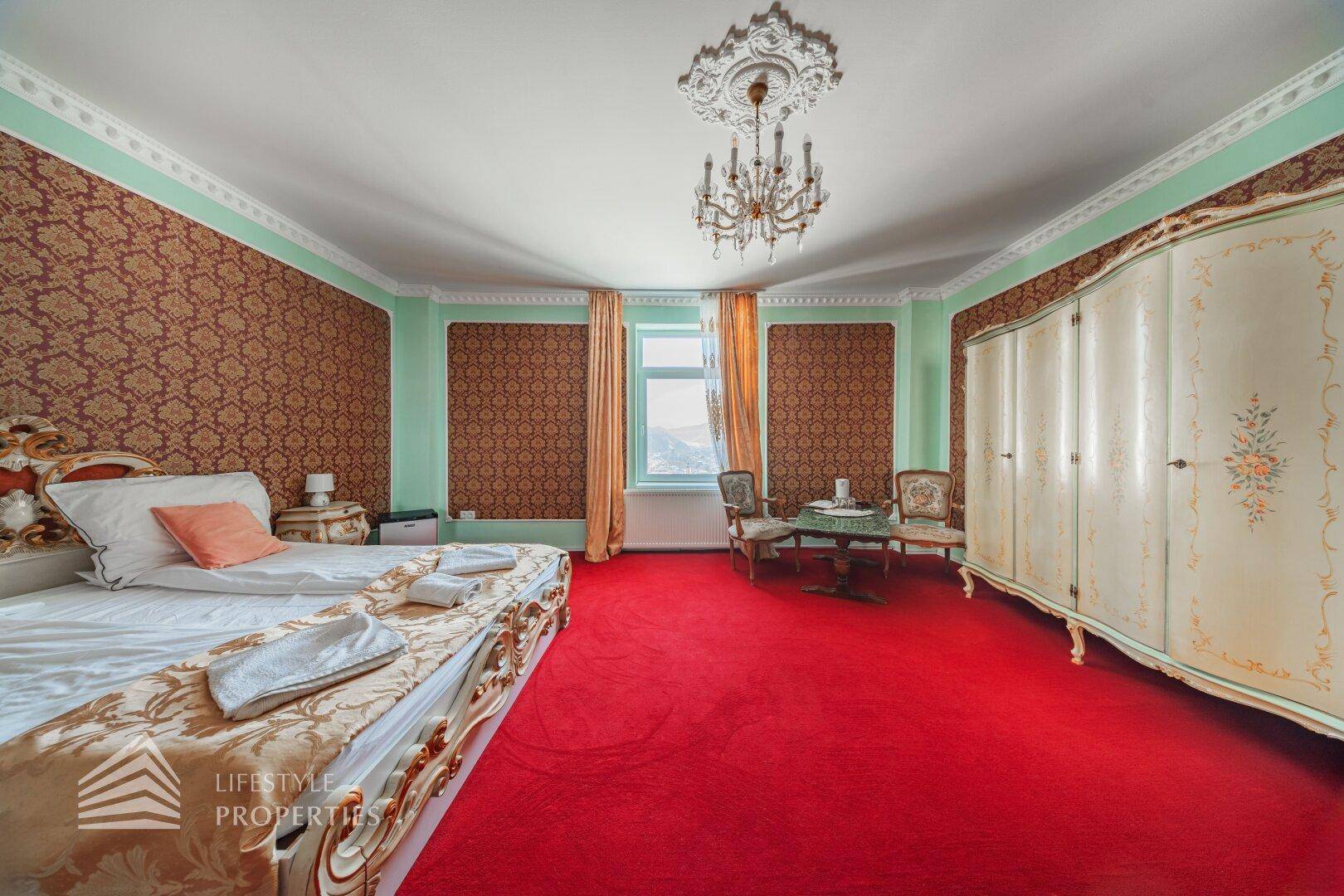 Geräumiges Schlafzimmer mit Doppelbett, weißem Kleiderschrank und kleiner Sitzecke am Fenster.