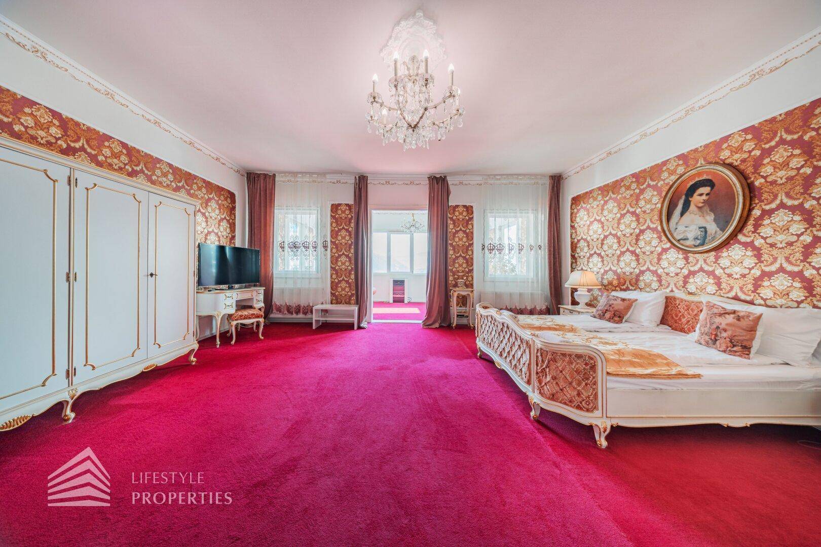 Geräumiges Schlafzimmer im klassischen Stil mit rotem Teppich, opulenten Tapeten und Kronleuchter.