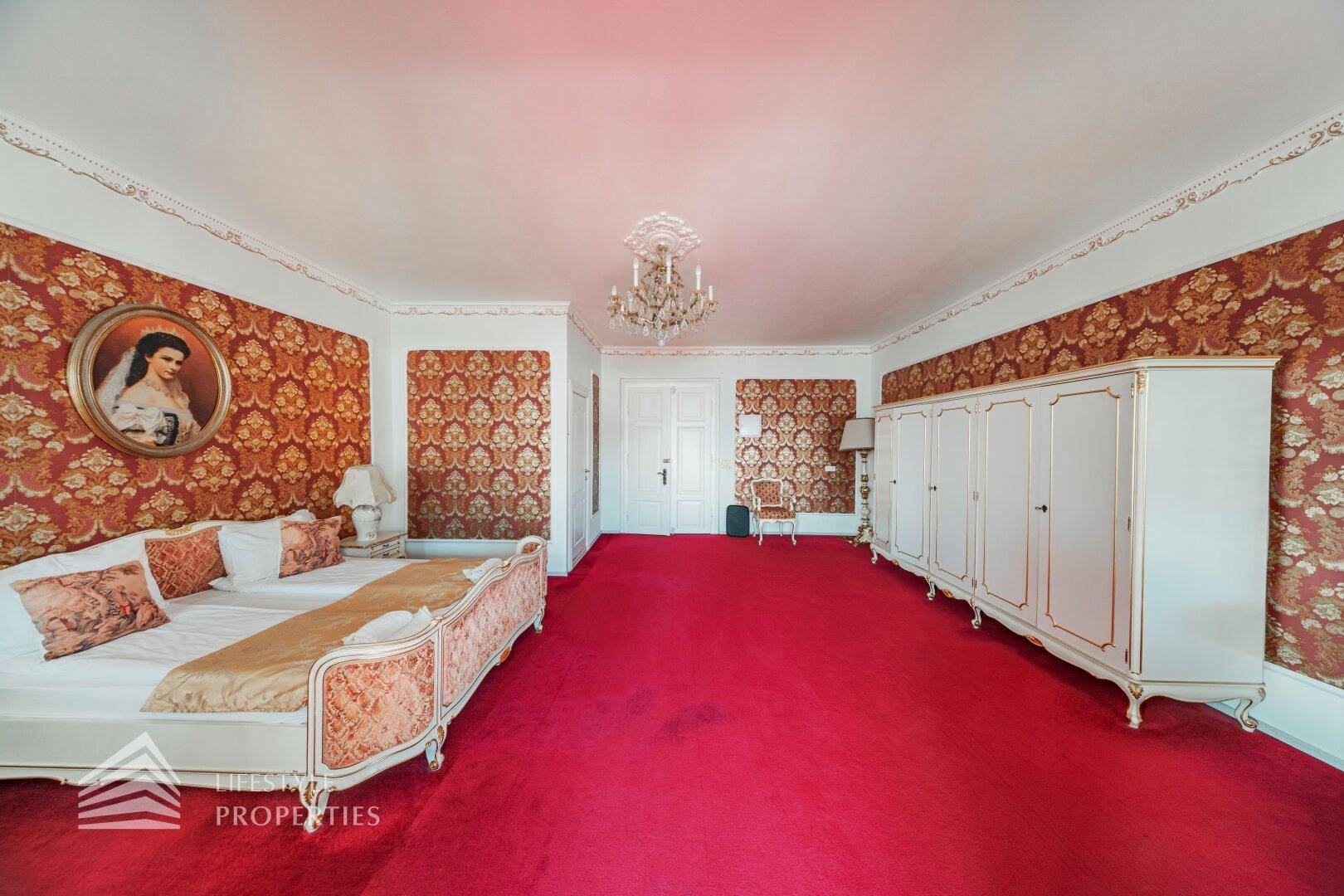 Klassisches Schlafzimmer mit rotem Teppich, opulentem Bett und weißem Kleiderschrank.