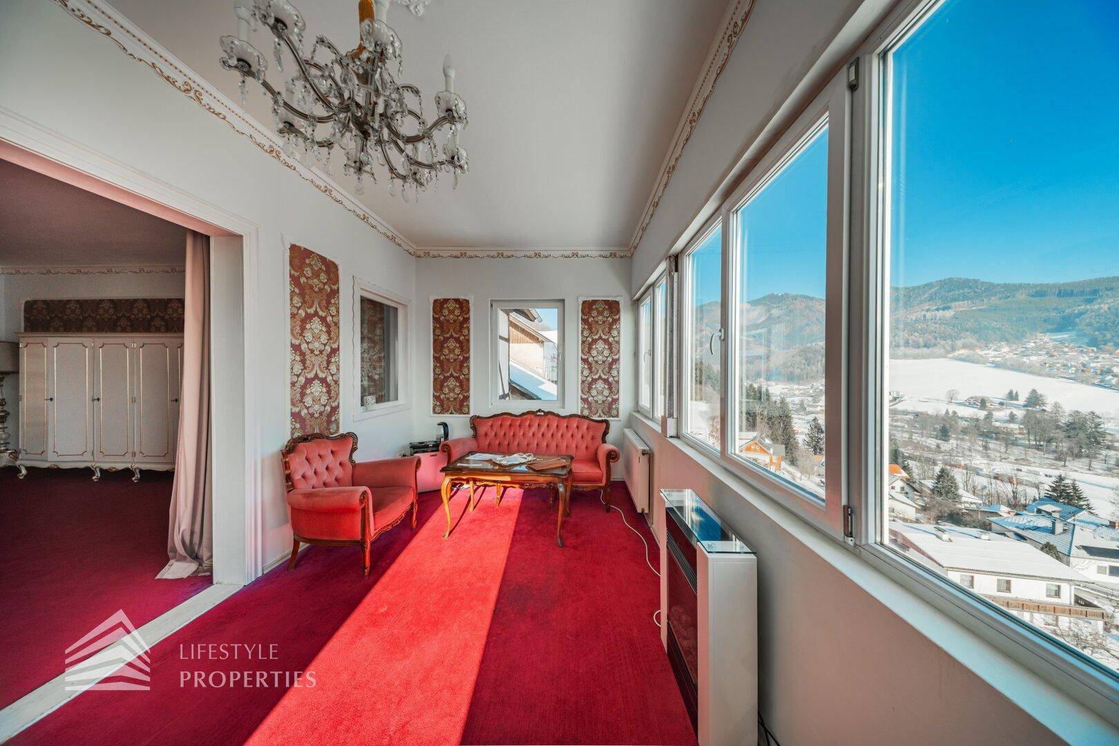 Helles Wohnzimmer mit rotem Teppich, klassischer Einrichtung und weitem Blick auf die Landschaft.