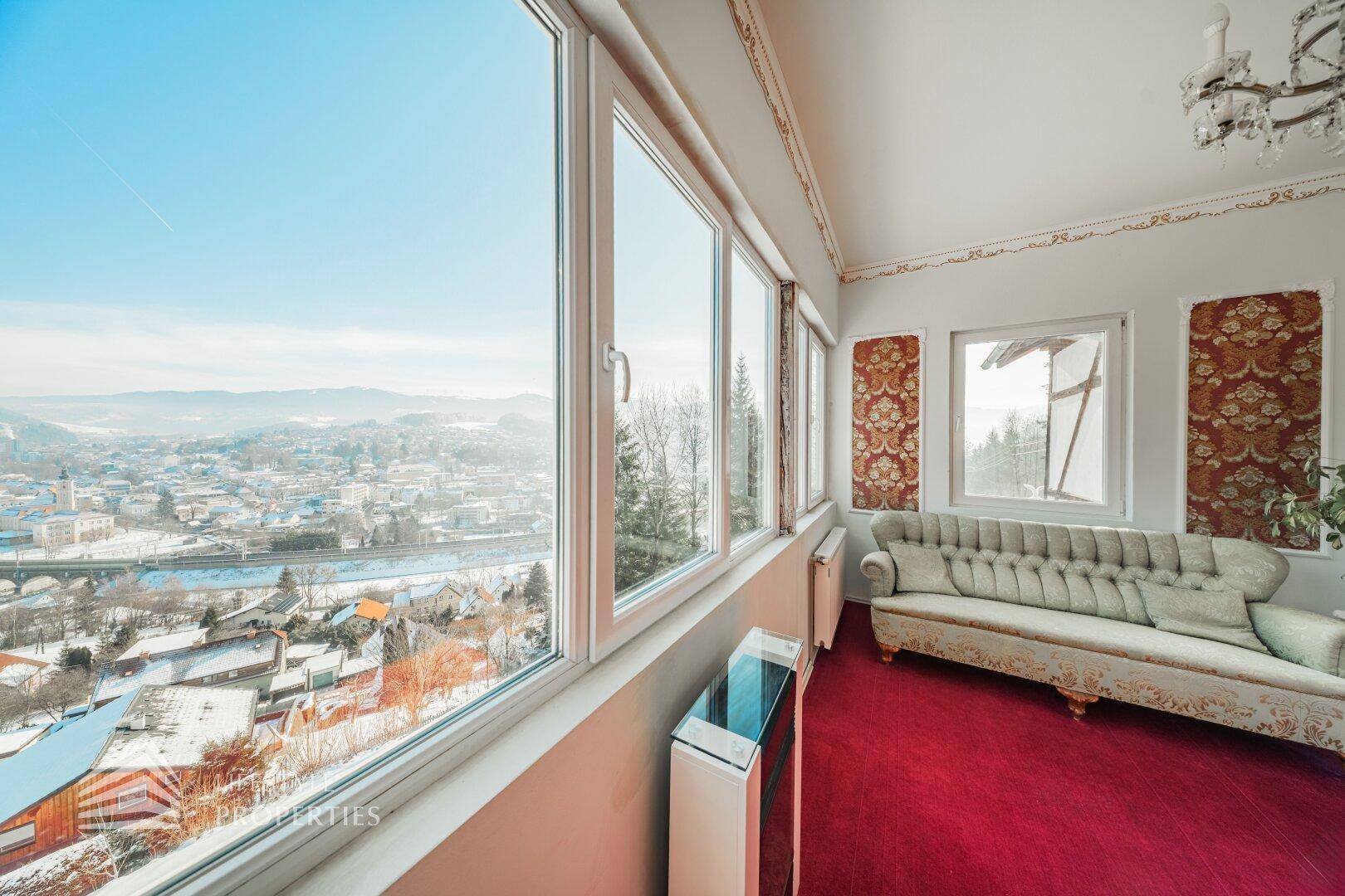 Geräumiges Wohnzimmer mit großen Fenstern, die einen Panoramablick auf die verschneite Landschaft bieten.