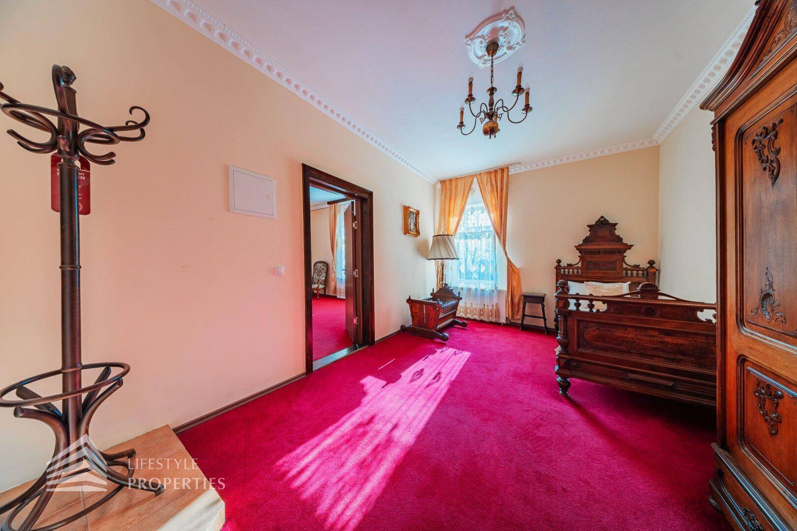 Schlafzimmer im traditionellen Stil mit rotem Teppich, dunklem Holzmobiliar und Kronleuchter.