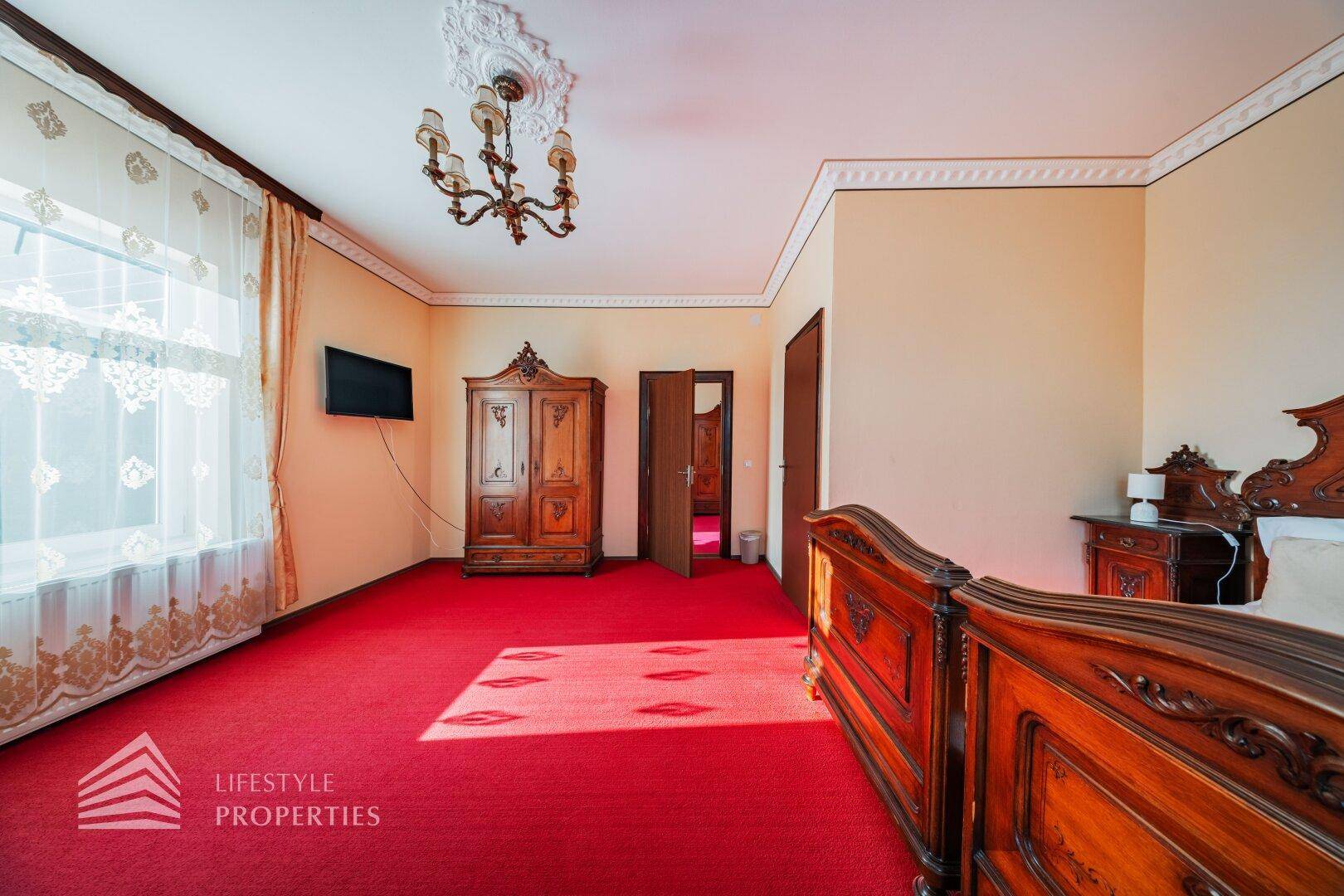 Geräumiges Schlafzimmer mit rotem Teppich, dunklem Holzschrank und traditioneller Einrichtung.
