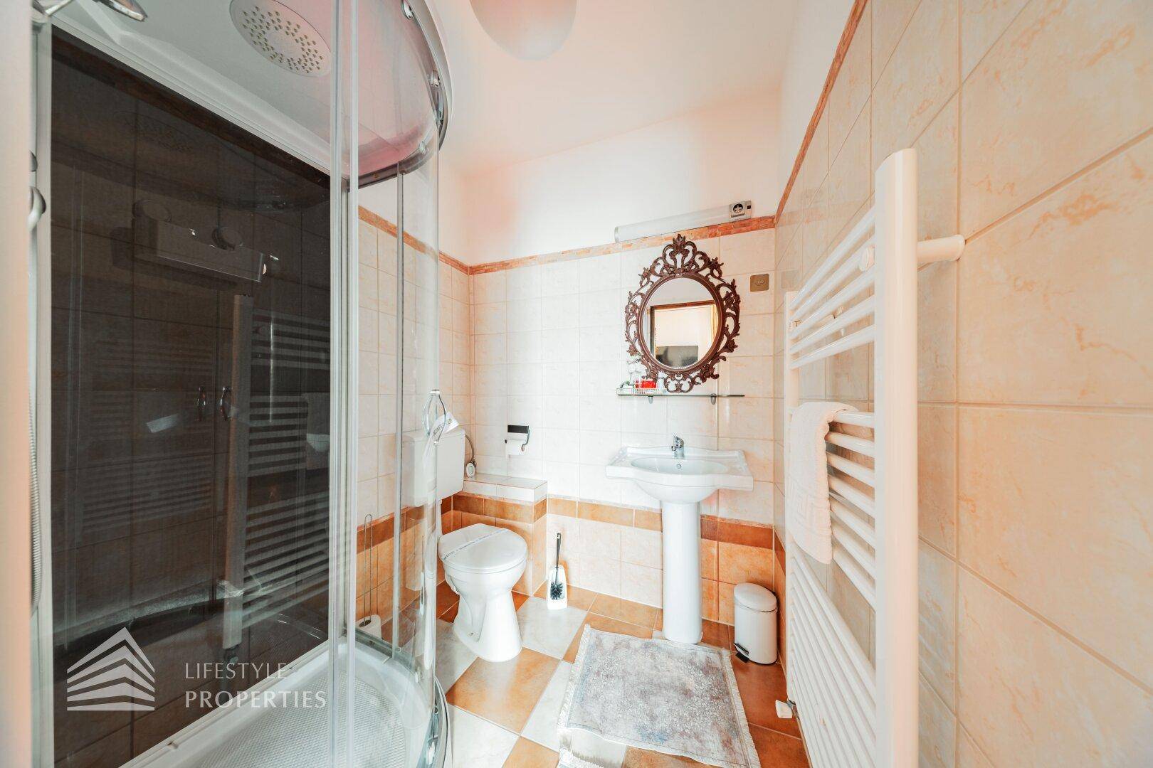 Badezimmer mit Duschkabine, Standwaschbecken und Fliesen in Beige- und Brauntönen.