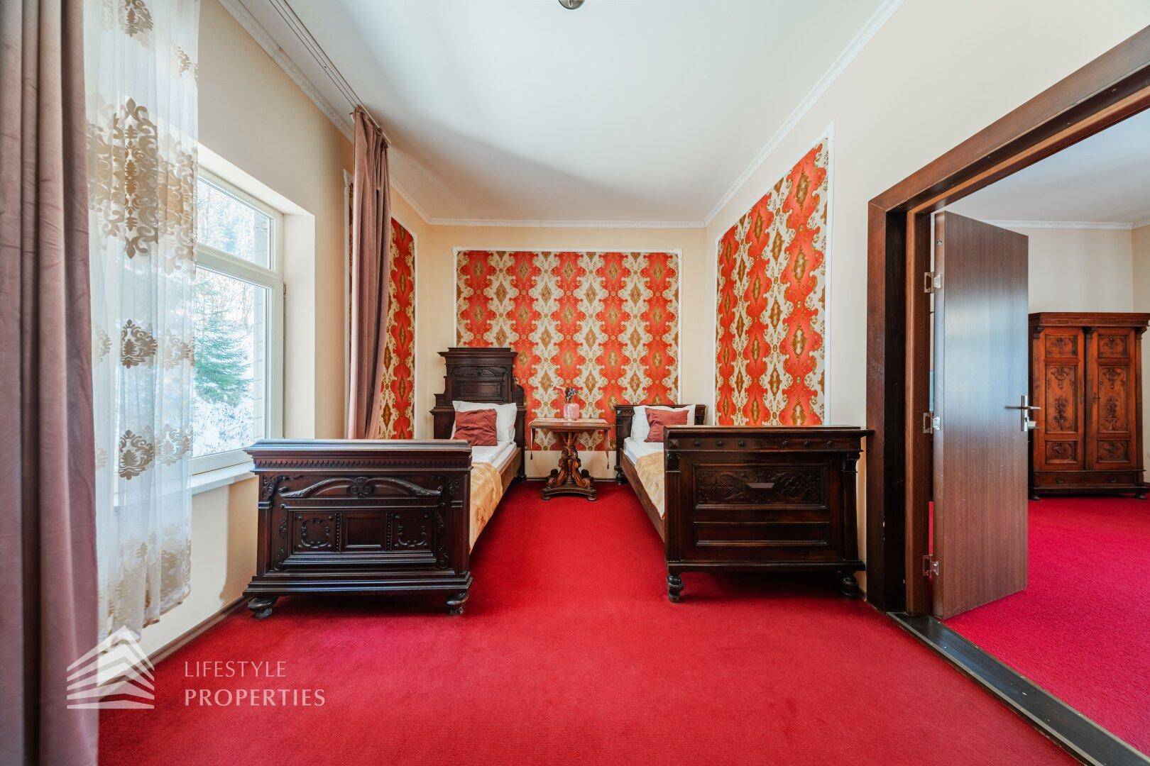Schlafzimmer mit zwei Einzelbetten, rotem Teppich und gemusterten Tapeten.