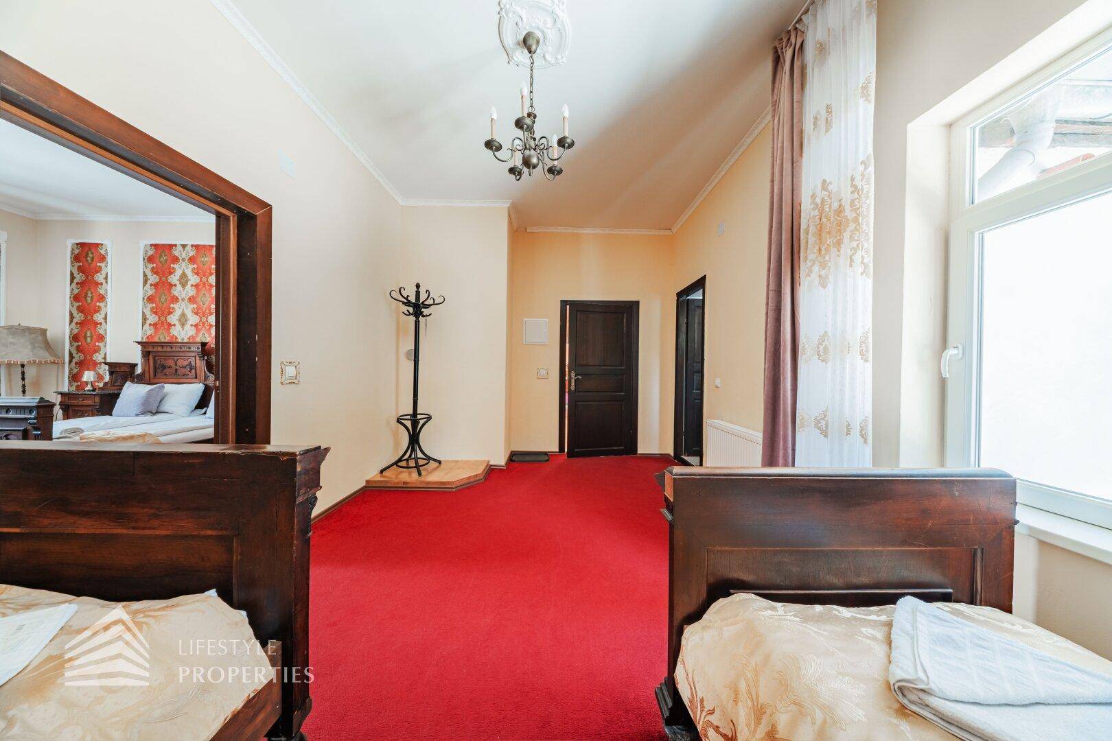 Schlafzimmer mit rotem Teppich, traditionellen Holzbetten und Zugang zum Flur.
