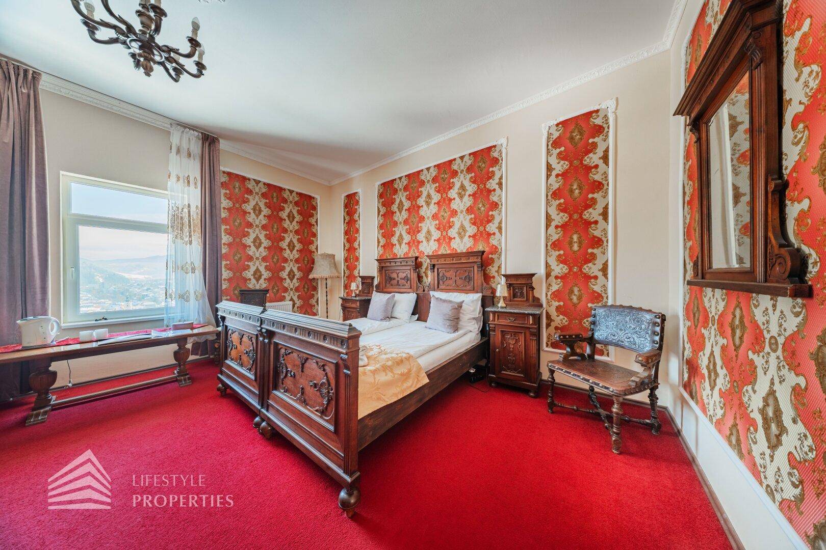 Großes Schlafzimmer mit rotem Teppich, dunklem Holzdoppelbett und gemusterter Tapete.