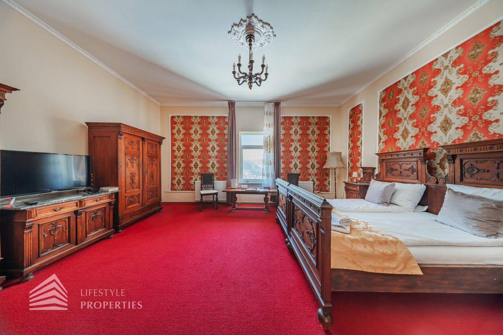 Geräumiges Schlafzimmer mit rotem Teppich, traditionellen Holzmöbeln und Blick ins Grüne.