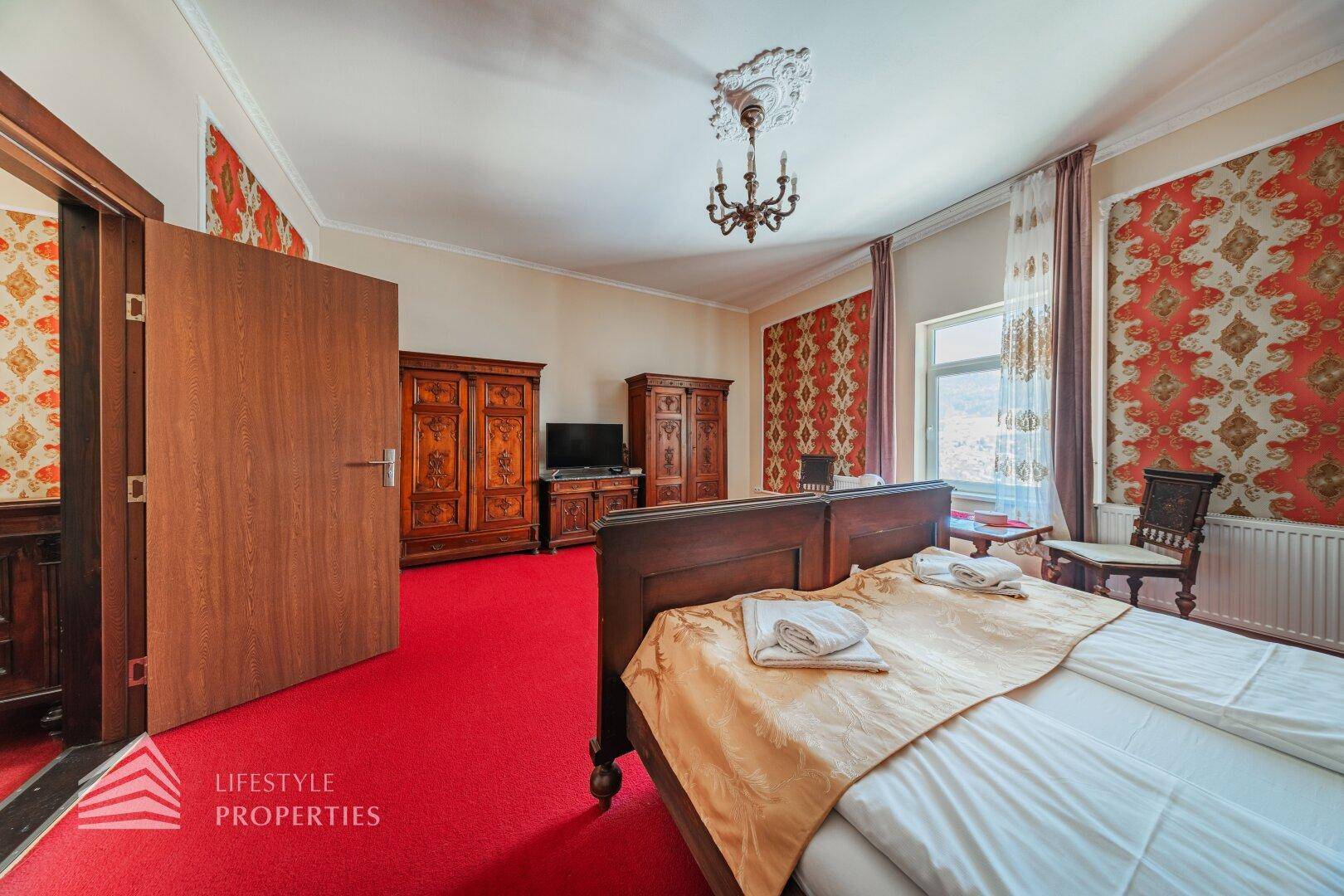 Schlafzimmer mit rotem Teppich, dunklem Holzschrank und traditionellem Doppelbett.