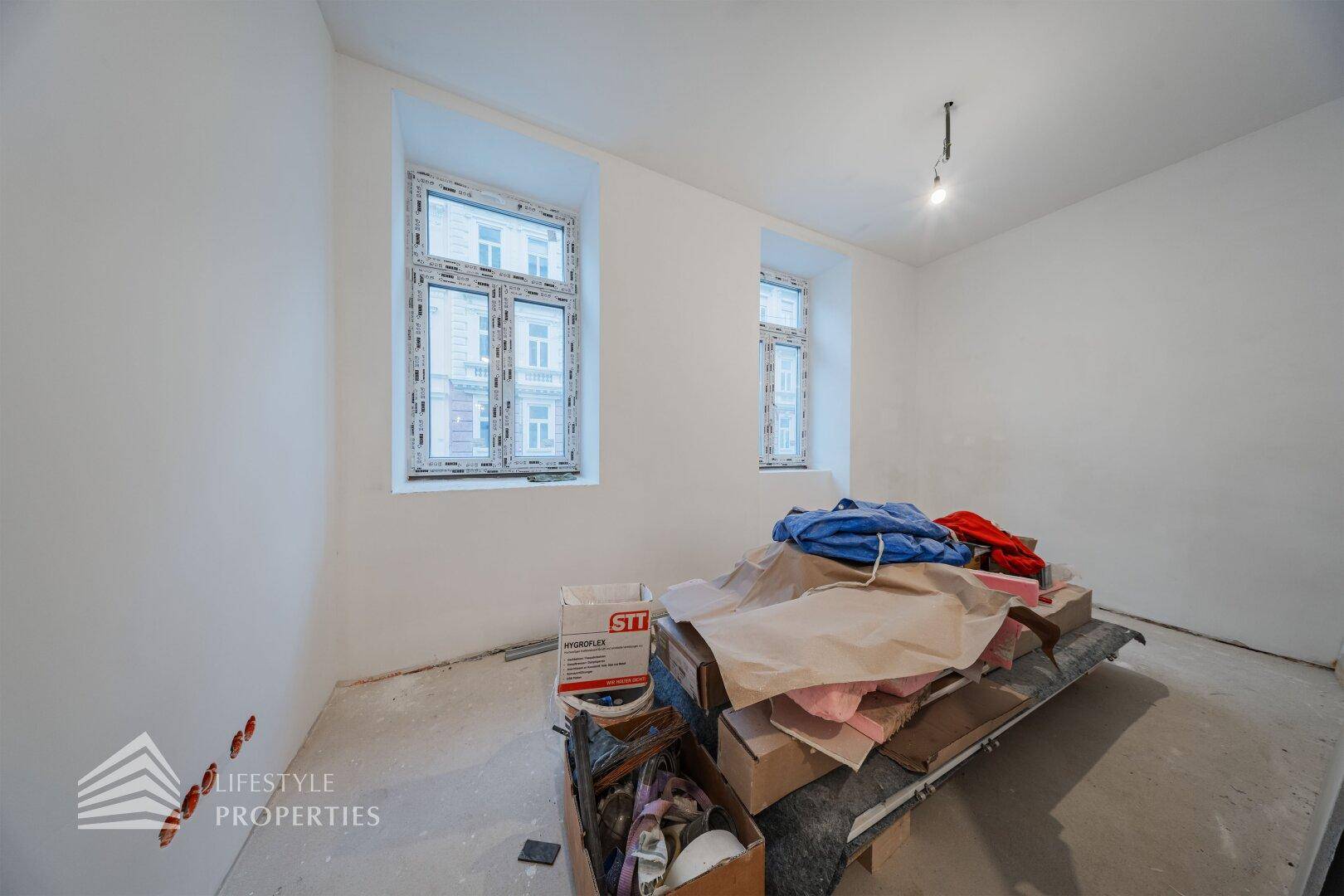 Leerer Raum im Rohbau mit zwei Fenstern, bereit für die weitere Gestaltung und Einrichtung.