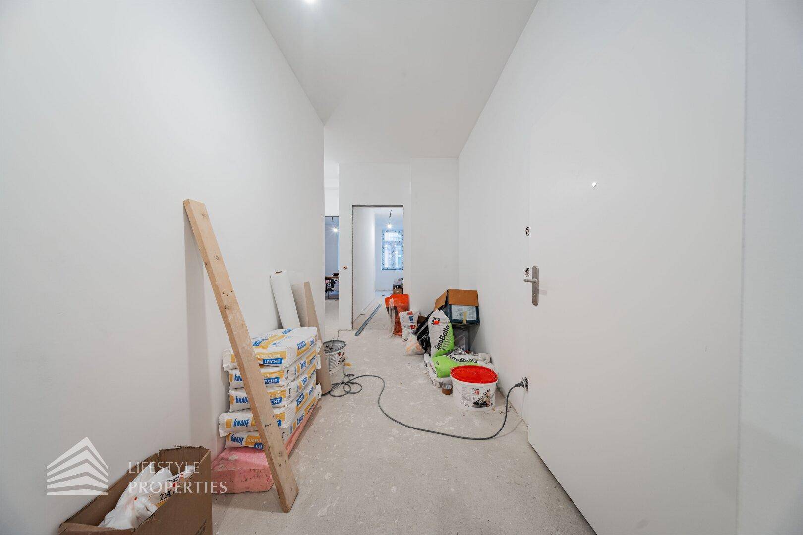 Heller Flur im Rohbau mit Baumaterialien und einer Eingangstür, bereit für den weiteren Ausbau.