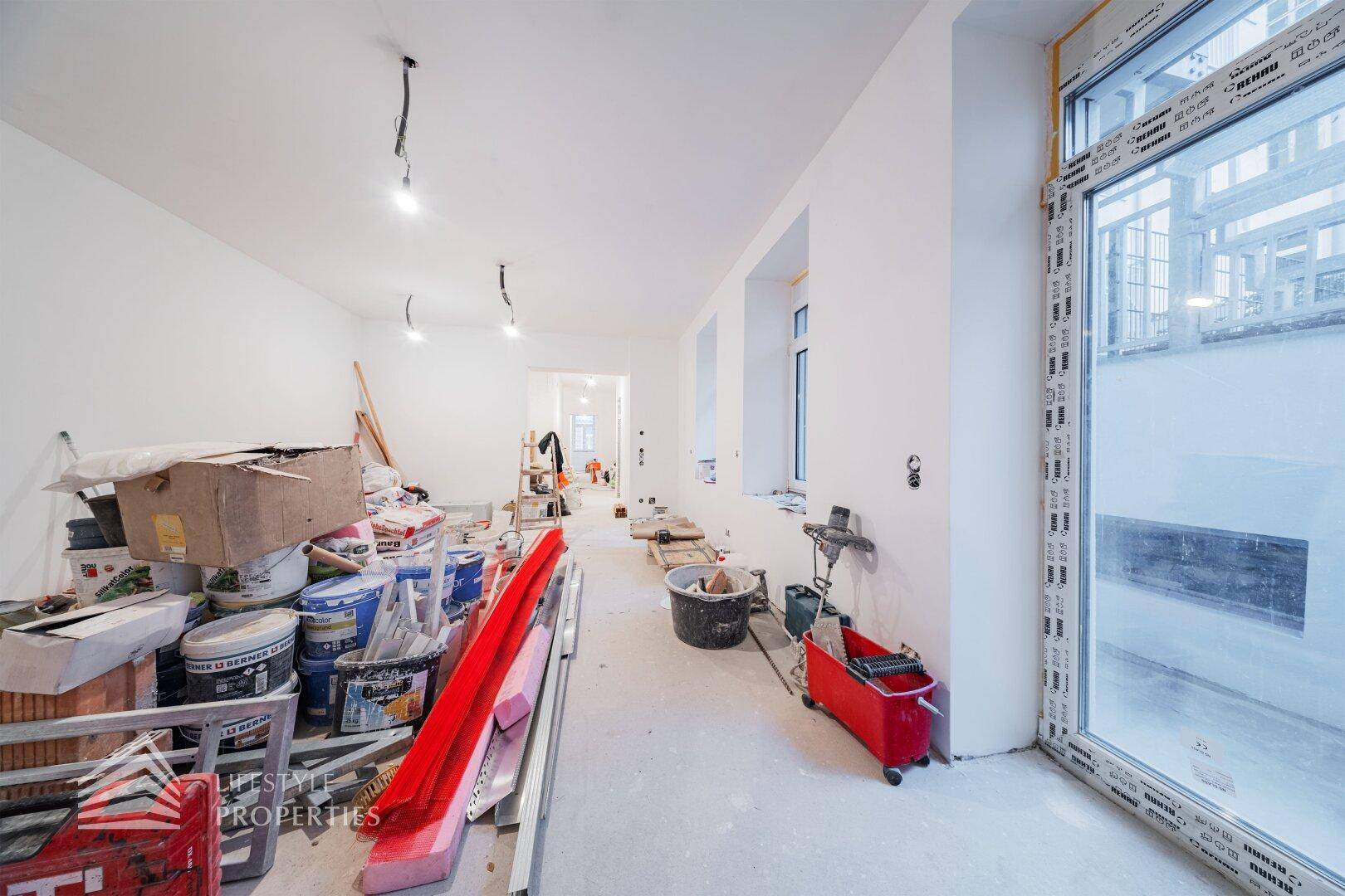 Großer Raum im Rohbau mit mehreren Fenstern und Baumaterialien, bereit für die Fertigstellung.
