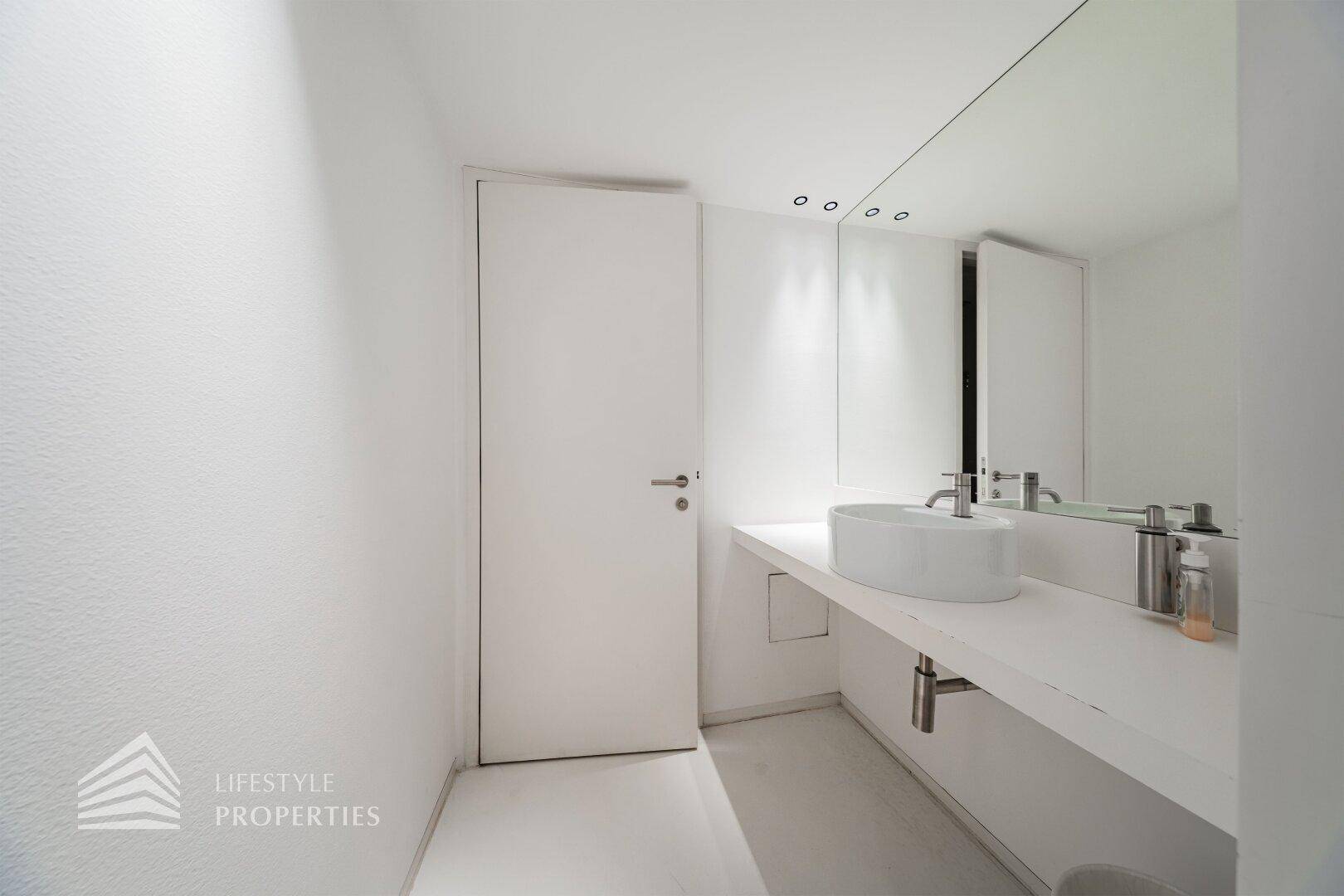 Modernes Badezimmer mit minimalistischem Design, rundem Waschbecken und großem Spiegel.
